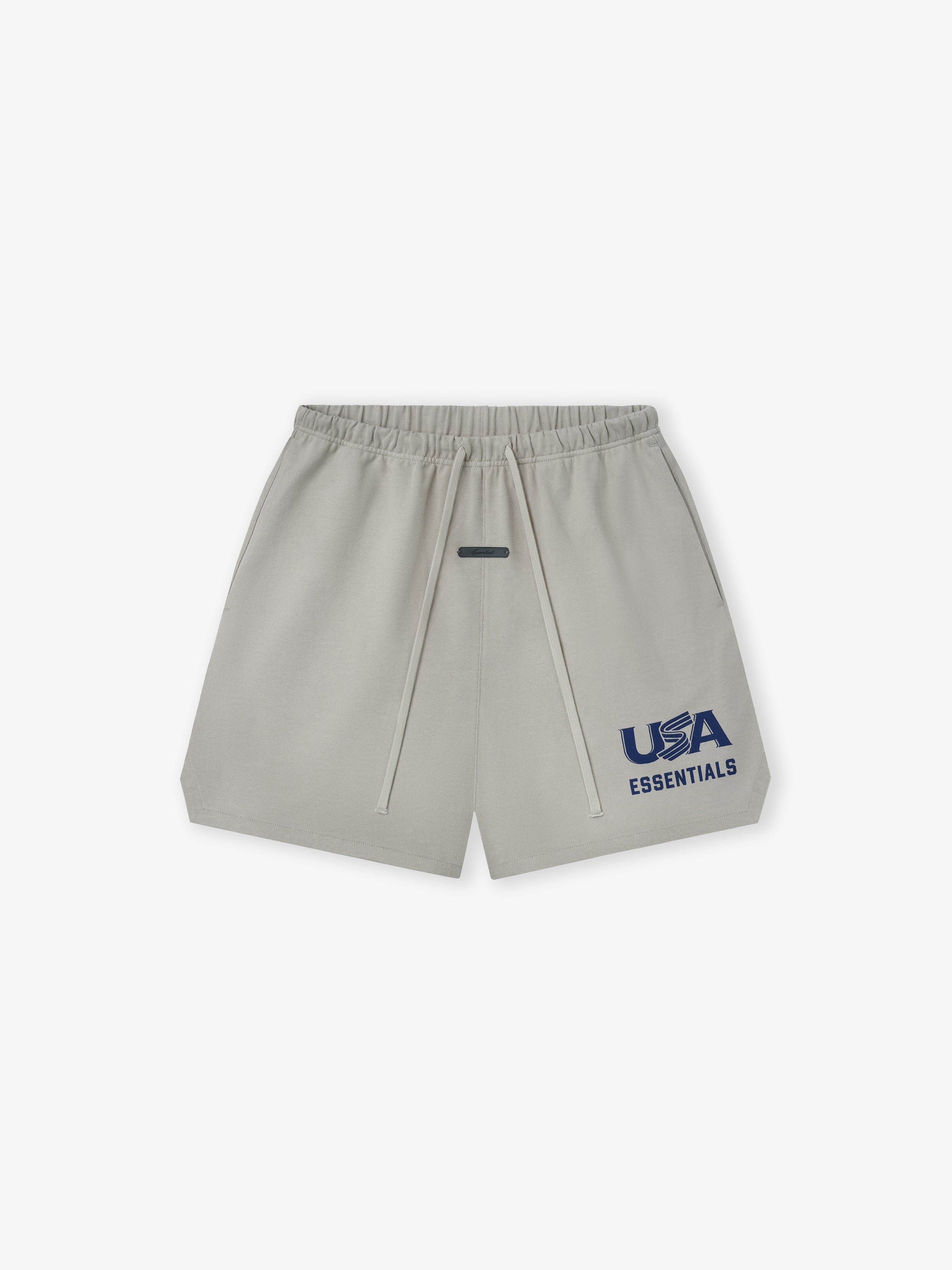 Light beige shorts with elastic waistband, drawstrings, and navy "USA ESSENTIALS" graphic on front left leg