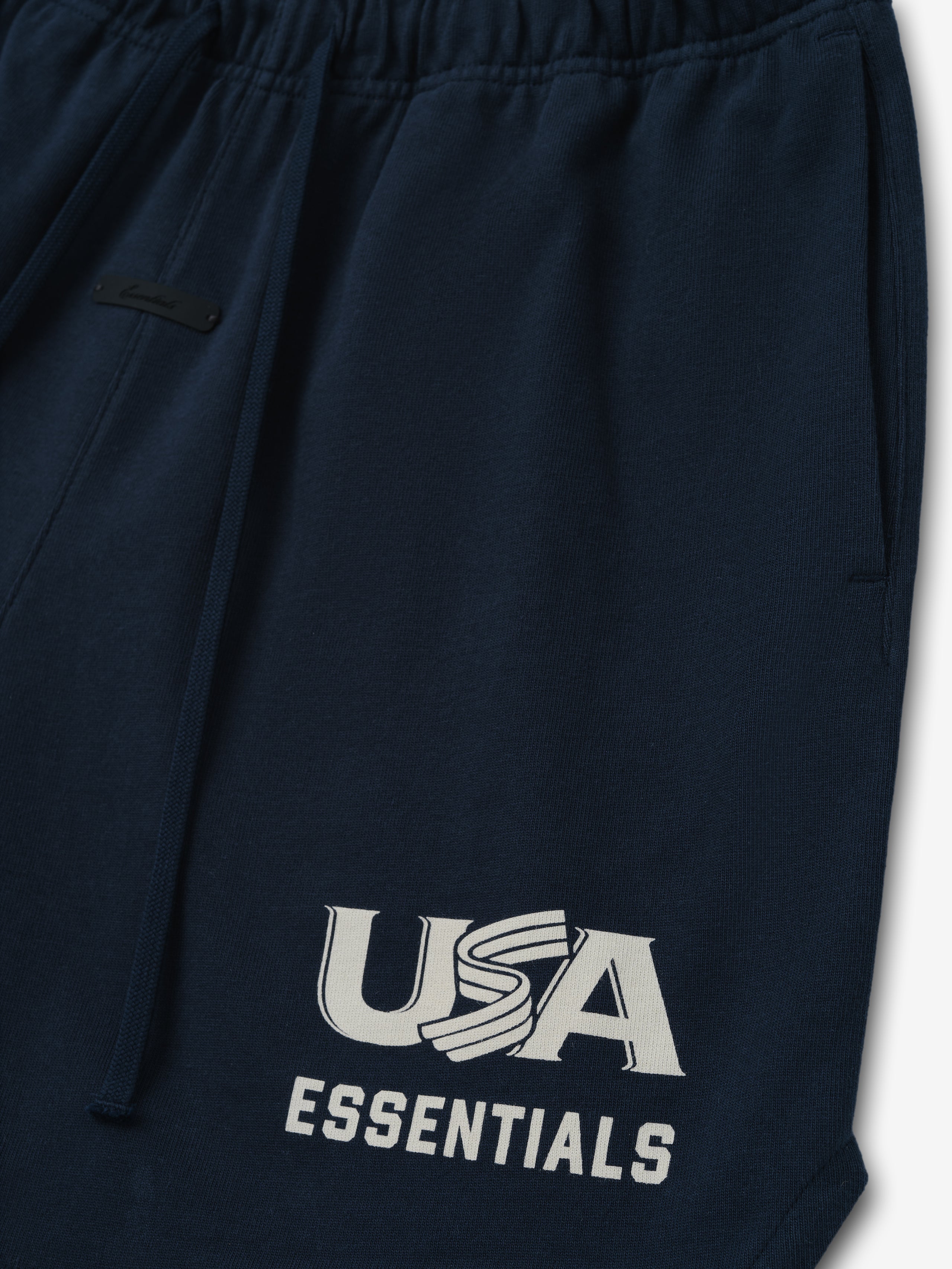 Close-up of dark navy sweatpants with elastic waistband, drawstring, side pocket, and white "USA ESSENTIALS" graphic on leg