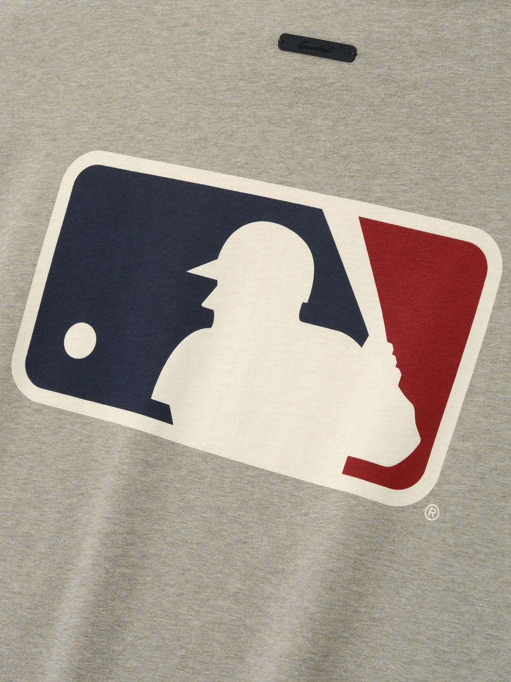 Close-up of a muted gray Mlb Merch Tee fabric featuring a large vintage-style baseball player silhouette logo in navy blue, cream, and deep red on a soft casual top.