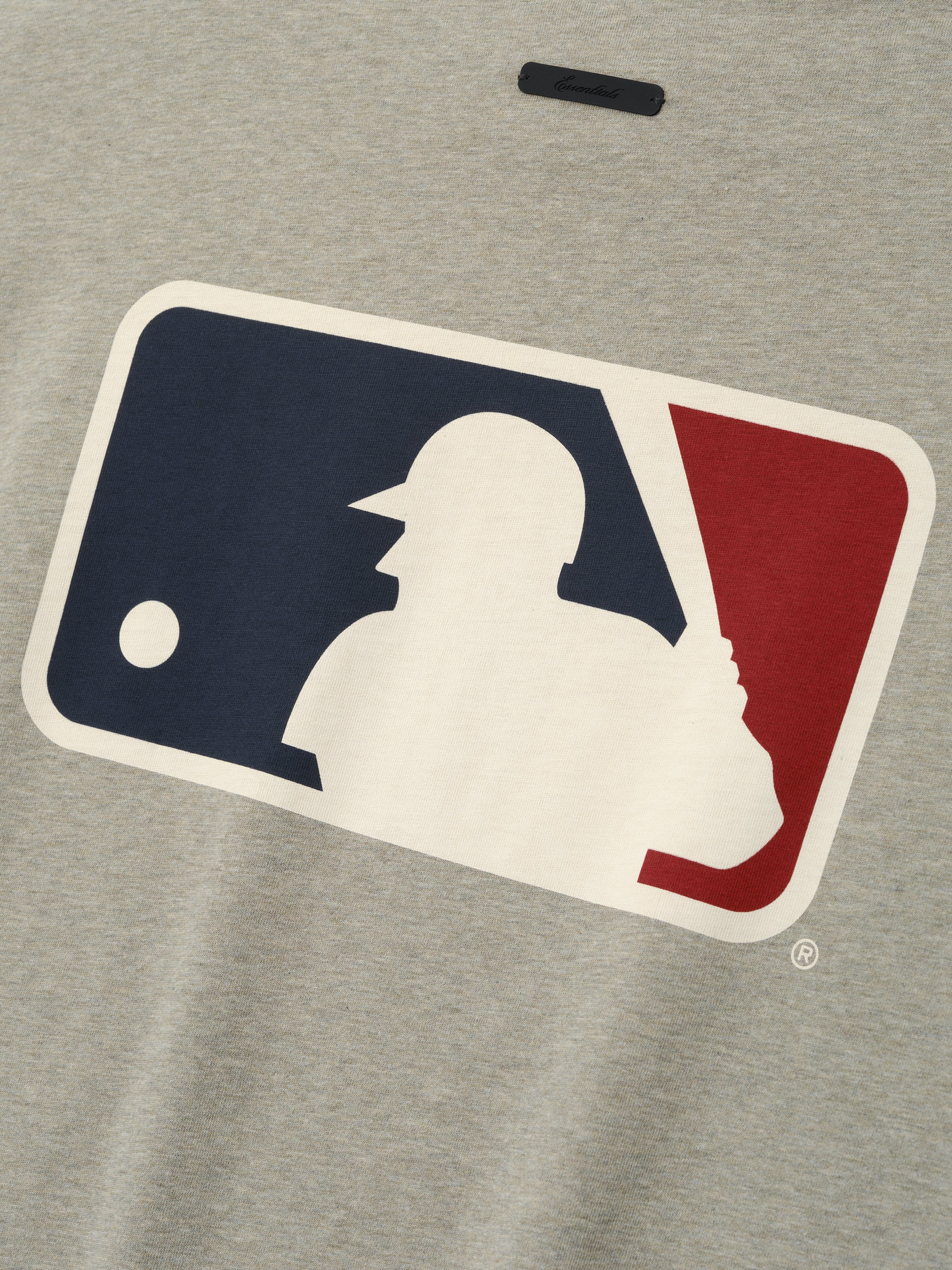 Close-up of a muted gray Mlb Merch Tee fabric featuring a large vintage-style baseball player silhouette logo in navy blue, cream, and deep red on a soft casual top.