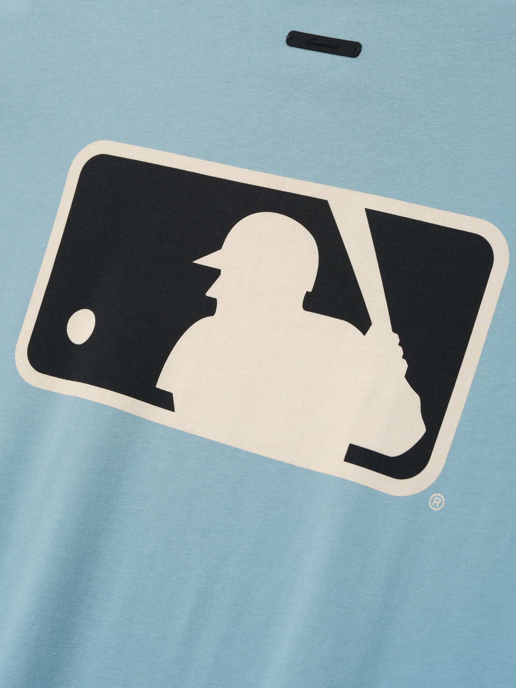 Close-up of stone blue Mlb Merch Tee fabric displaying a large contrasting cream and black graphic of a baseball batter silhouette with a ball approaching.