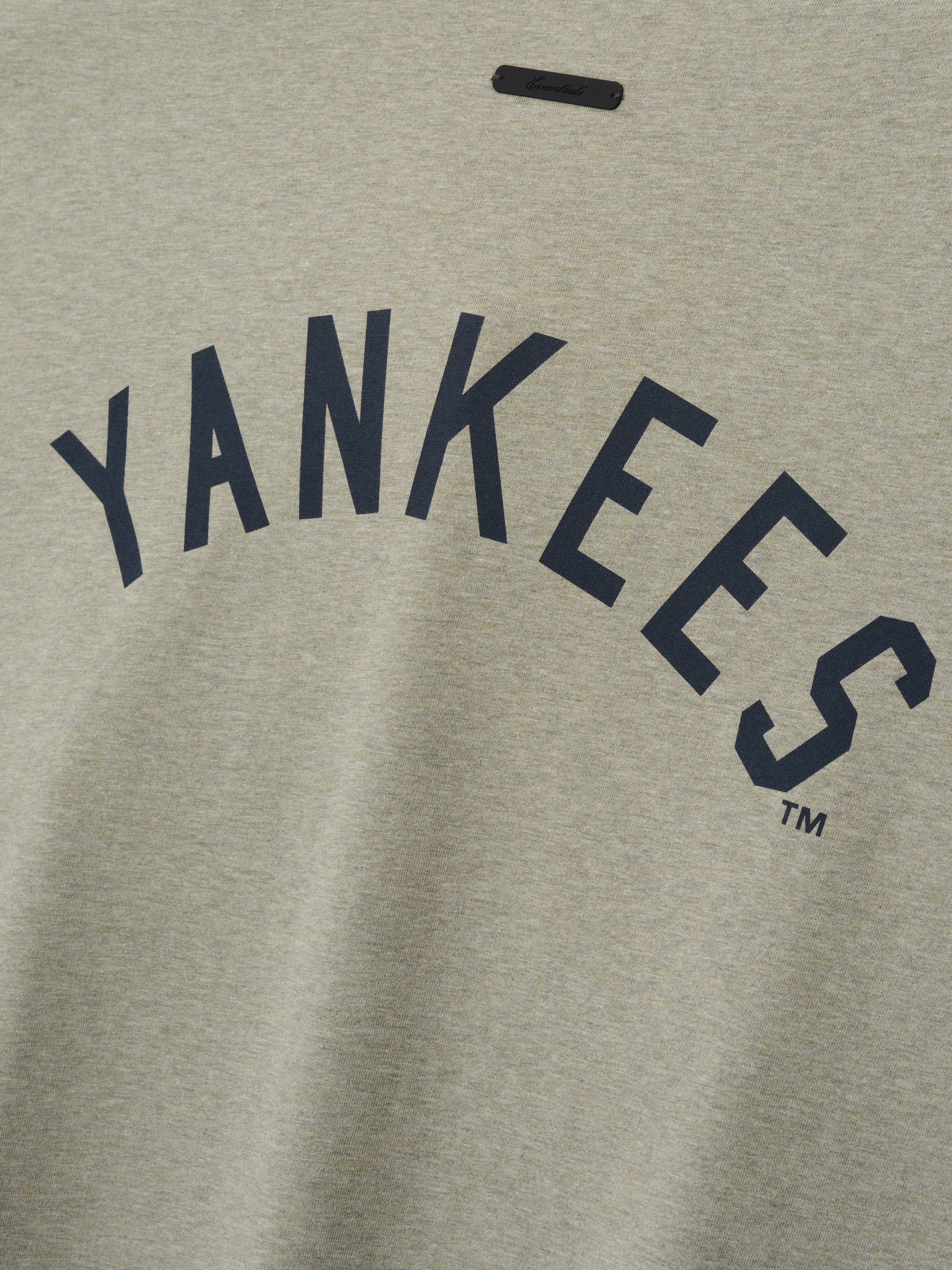 Close-up of a beige heather Yankees Merch Tee featuring bold navy blue "YANKEES" text printed in an arched style across soft cotton fabric.