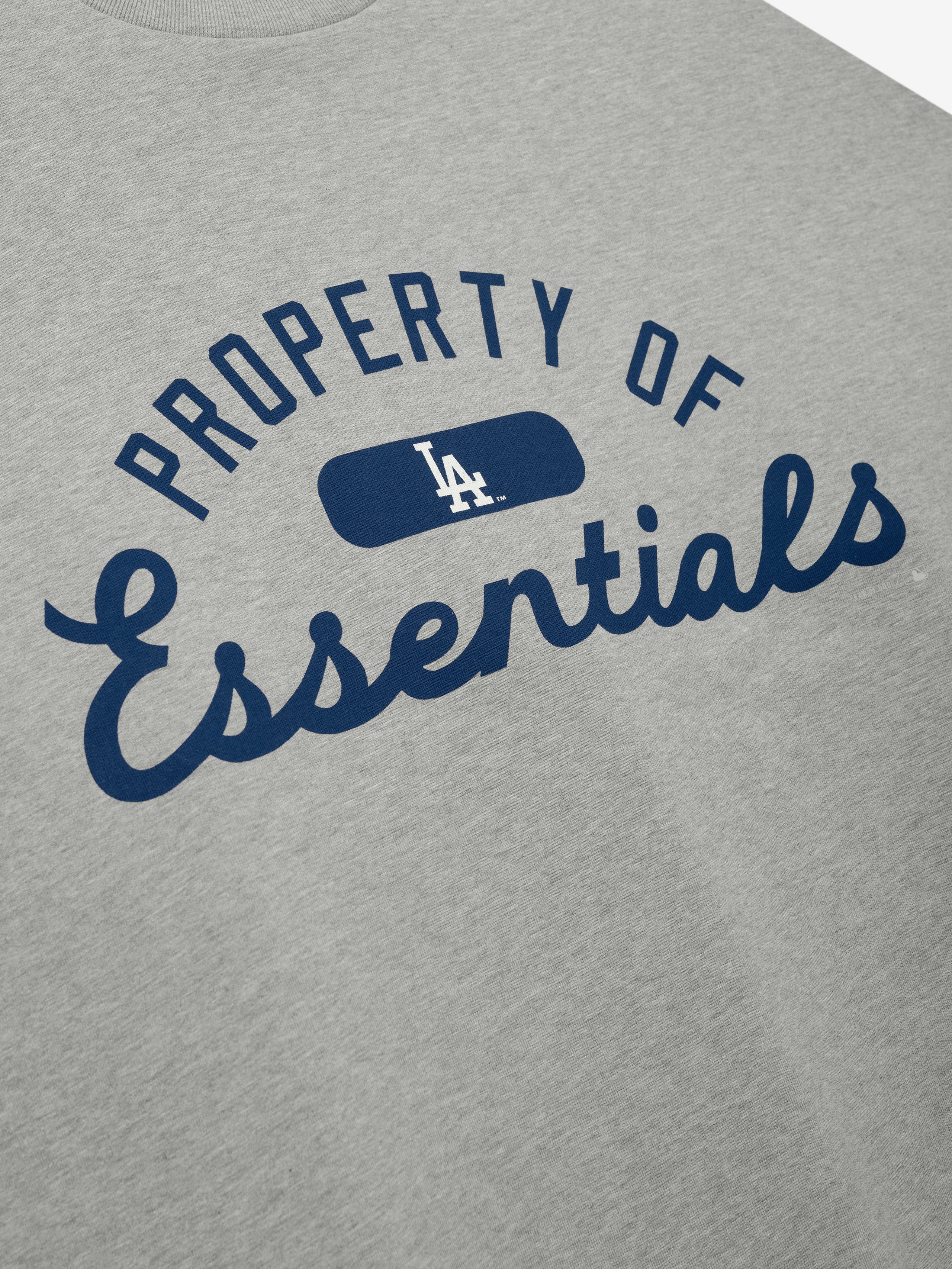 Dodgers Merch Tee in light gray fabric featuring navy blue "Property of Essentials" text with a small LA logo centered, designed as a casual, comfortable top.