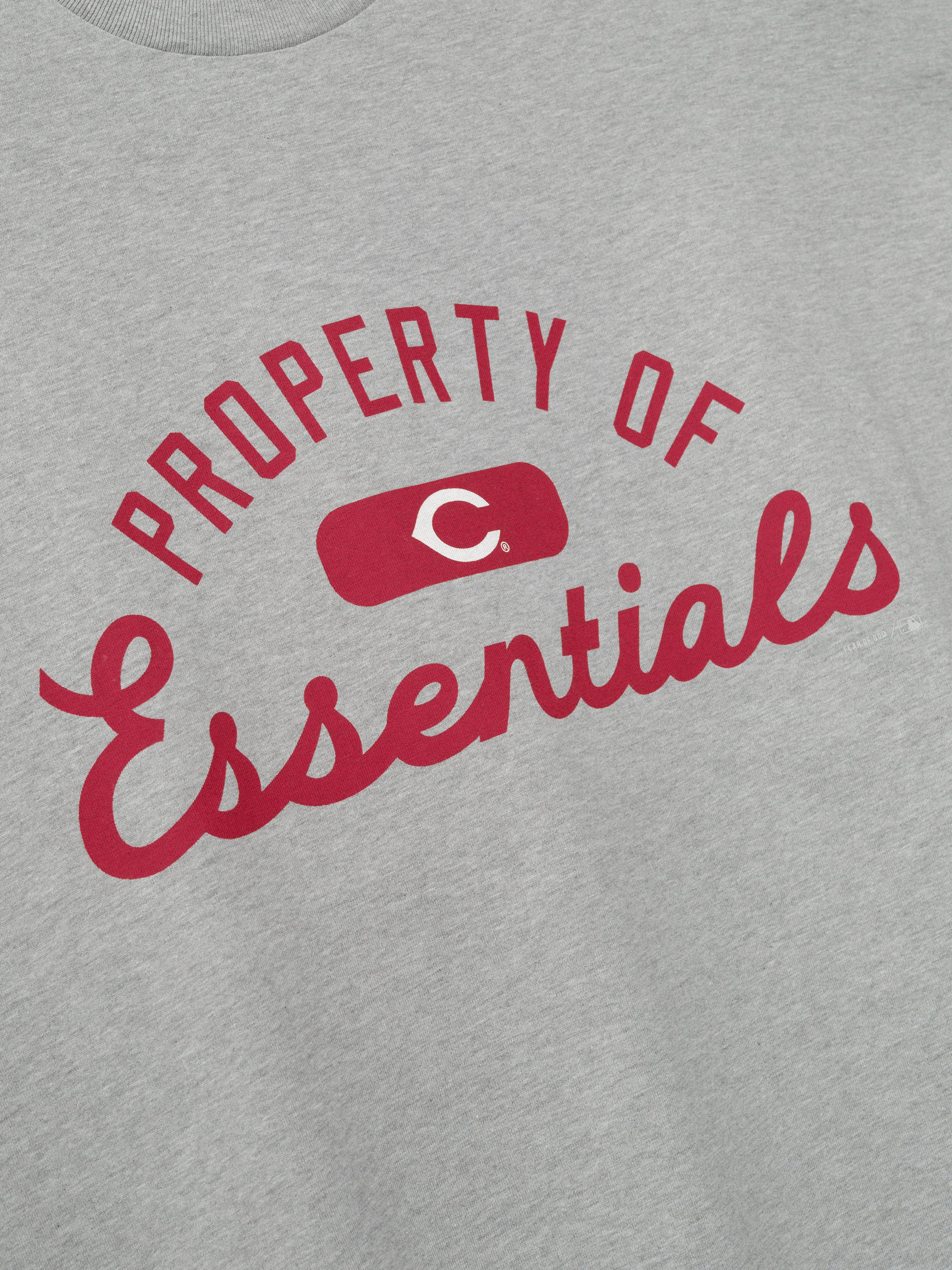 Reds Merch Tee in a soft, light gray fabric featuring bold red "PROPERTY OF Essentials" lettering with a centered red graphic emblem, designed as a casual, comfortable top.