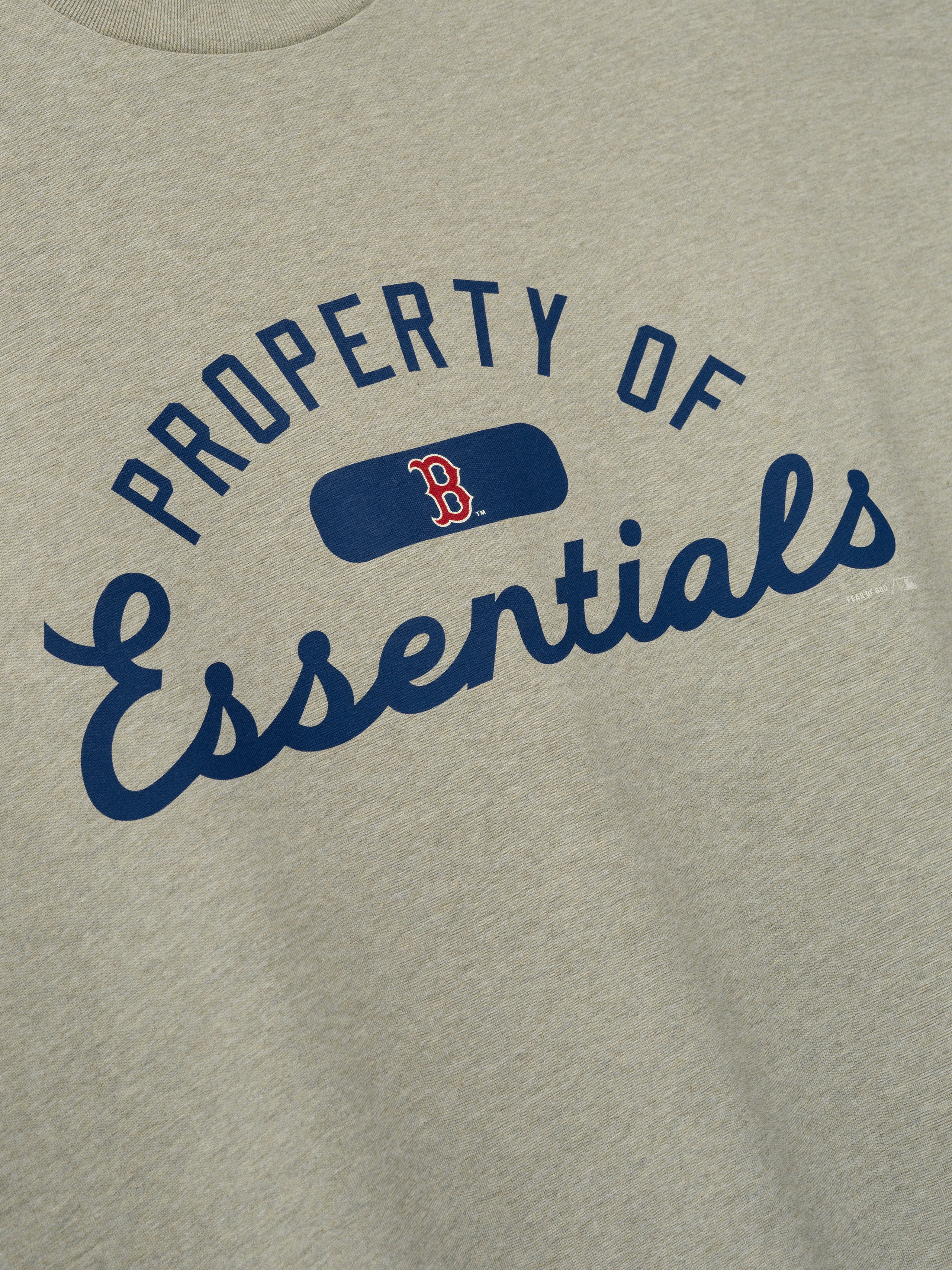Close-up of the Red Sox Merch Tee in a muted heather tone featuring navy blue "Property of Essentials" text with a small red and navy Boston "B" logo on soft cotton fabric.