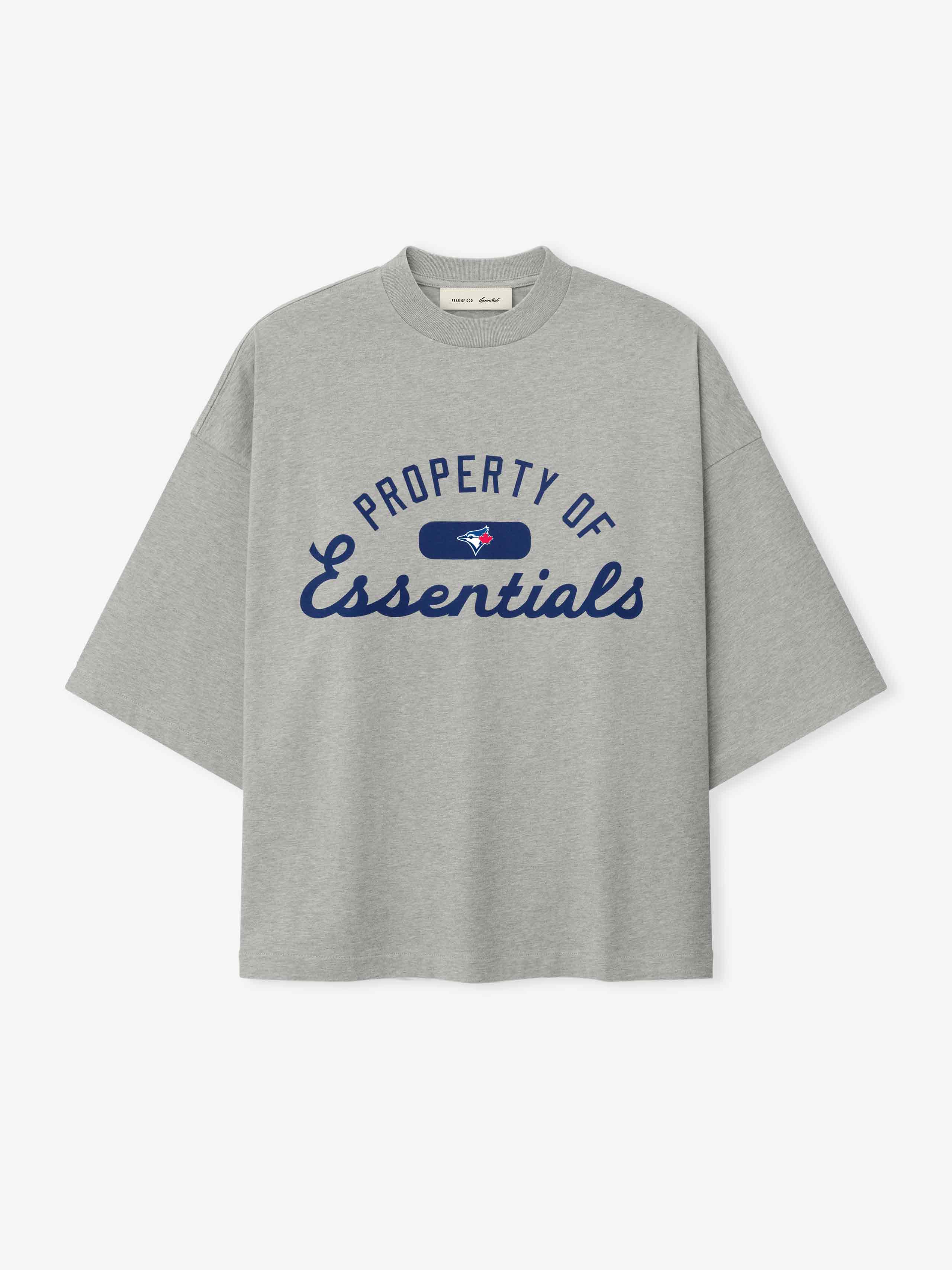 Blue Jays Merch Tee in a light heather gray shade featuring navy blue "Property of Essentials" script text and a small blue jay logo on a soft cotton top.