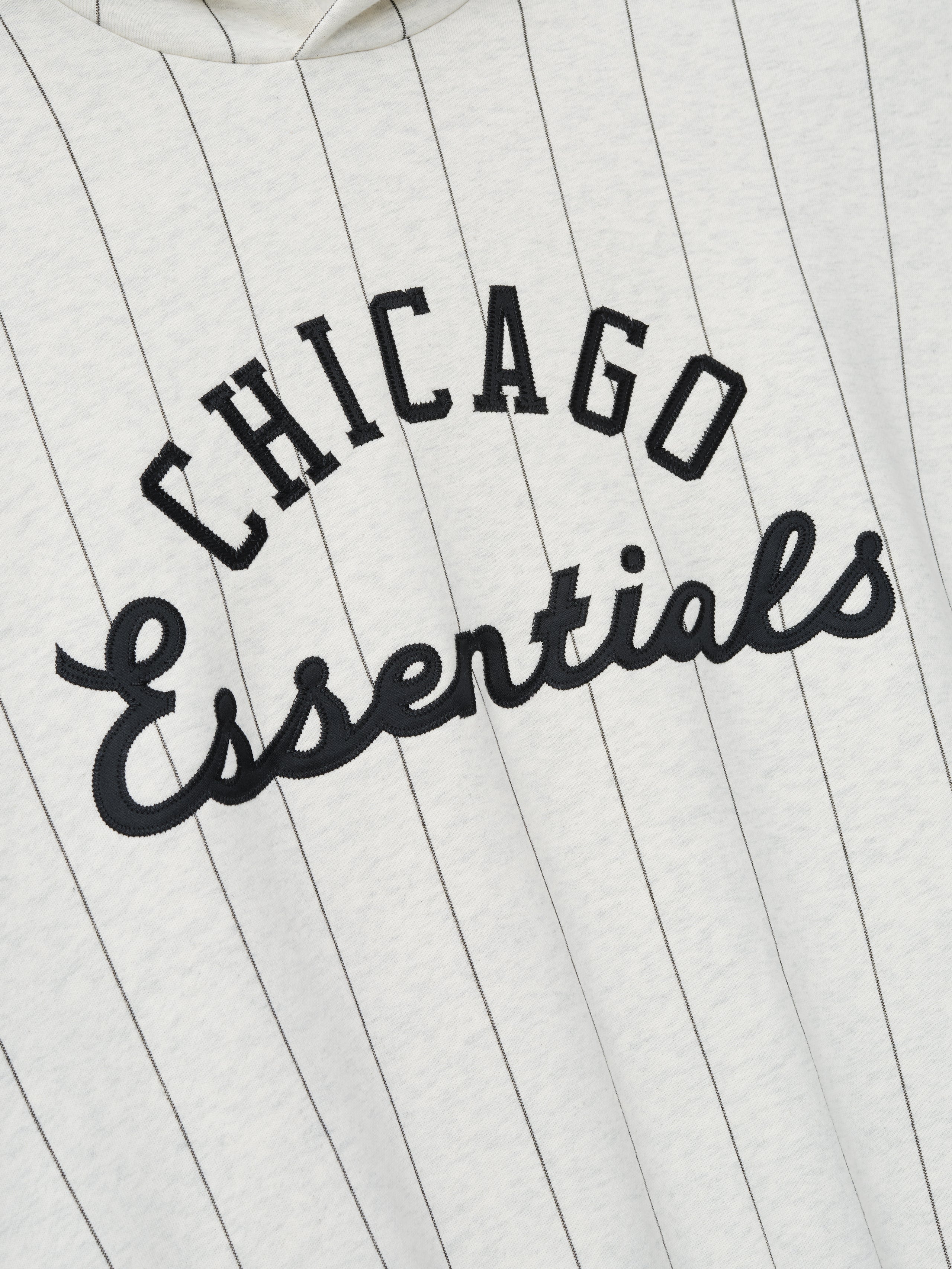 Close-up of the front of White Sox Sport Hoodie in oatmeal heather with thin black pinstripes and black embroidered "Chicago Essentials" text across the chest.