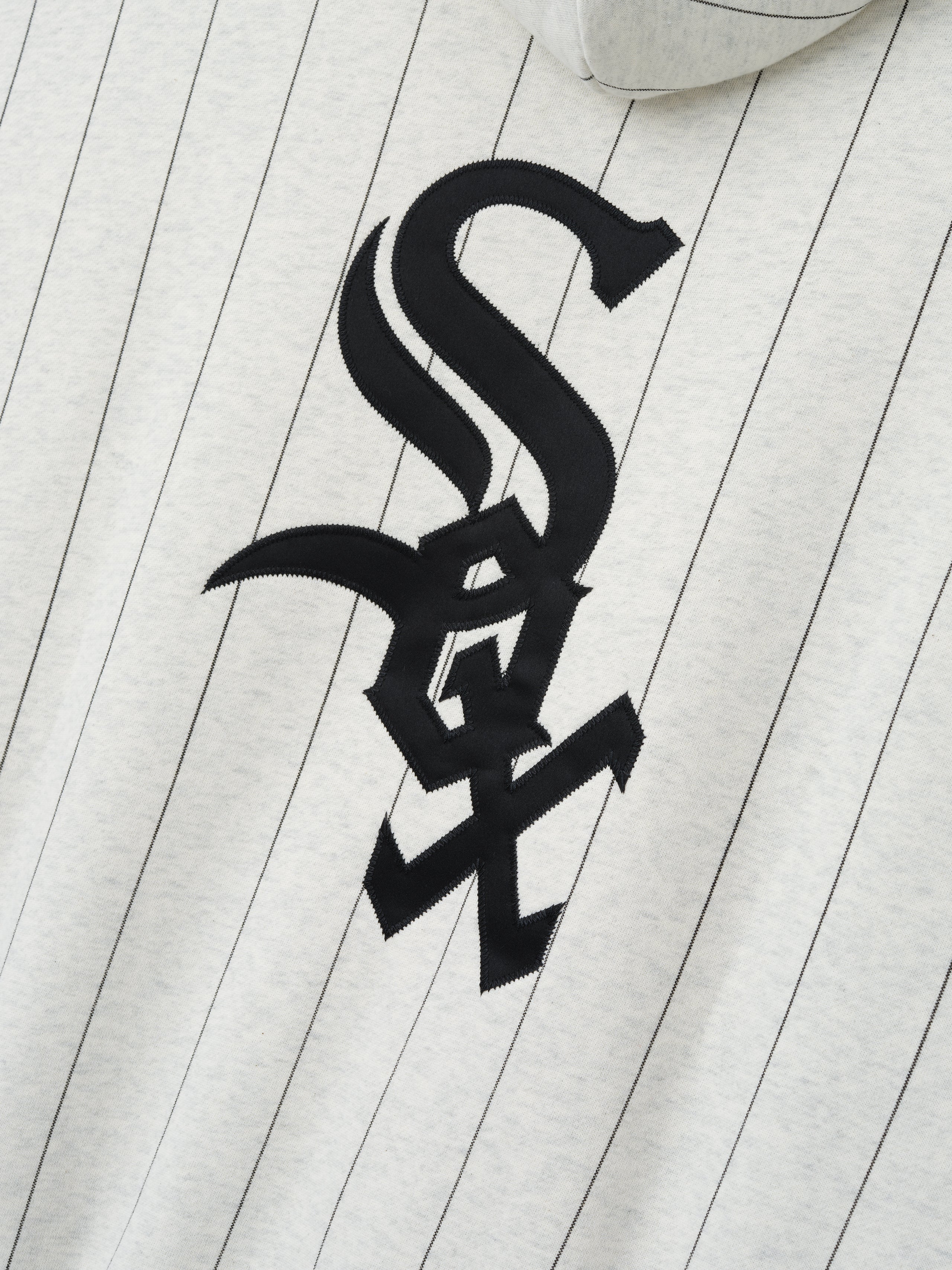 Close-up of the White Sox Sport Hoodie in oatmeal heather with thin black pinstripes and a large black embroidered stylized team logo on the front, made from soft fabric.