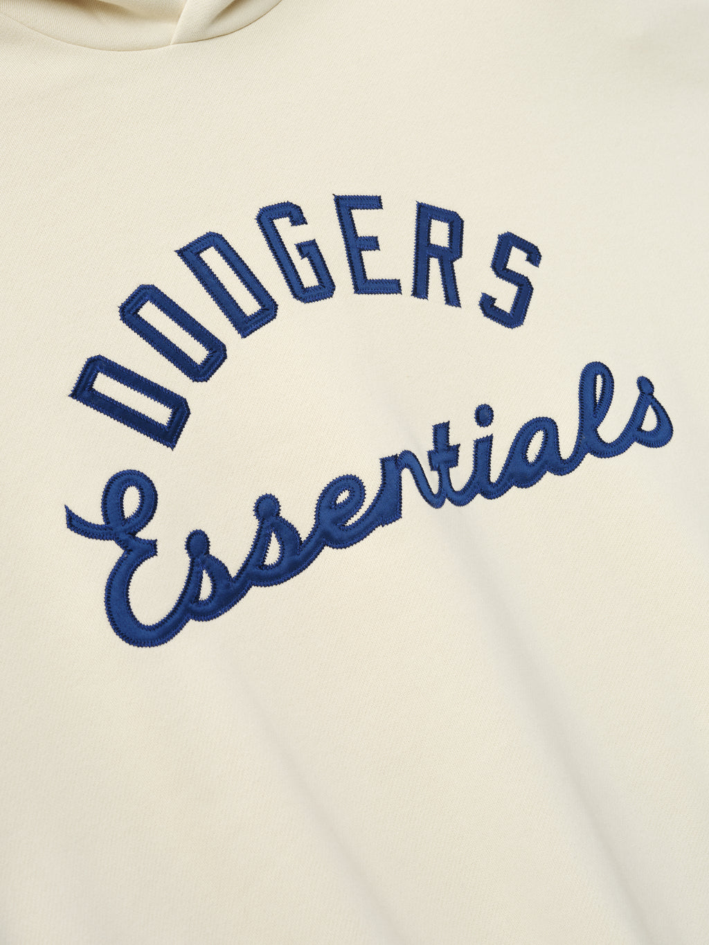 Close-up of cream Dodgers Sport Hoodie featuring raised navy blue embroidered "Dodgers Essentials" text on soft fabric, highlighting detailed stitching and sporty outerwear style.