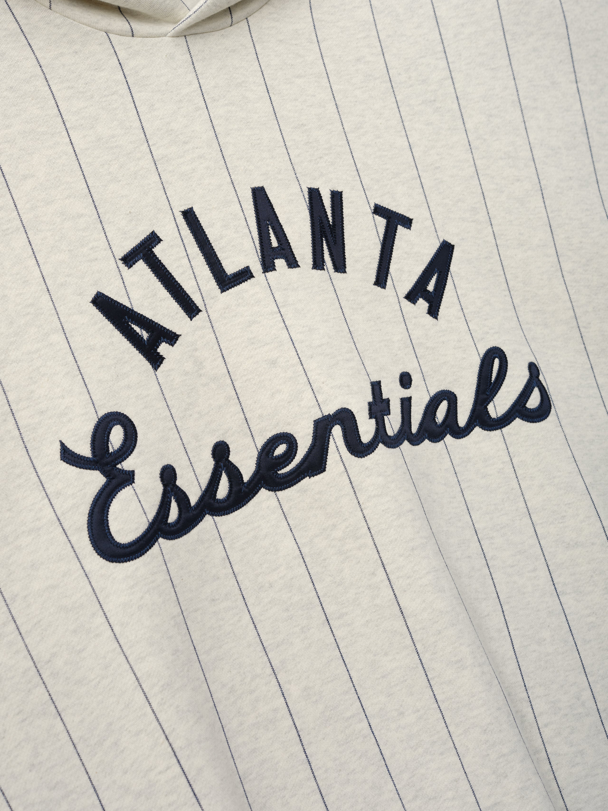 Braves Sport Hoodie in a soft oatmeal heather color with thin dark sapphire pinstripes and raised navy blue "Atlanta Essentials" embroidery in a mix of block and script fonts on cozy outerwear fabric.