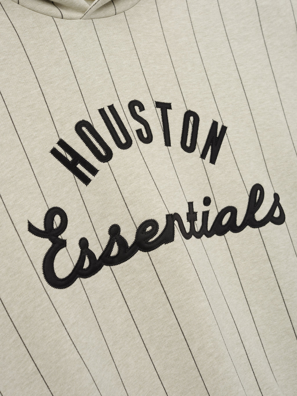 Close-up of Astros Sport Hoodie in a heather stone shade with thin black pinstripes, featuring bold black "HOUSTON Essentials" embroidered text on soft outerwear fabric.