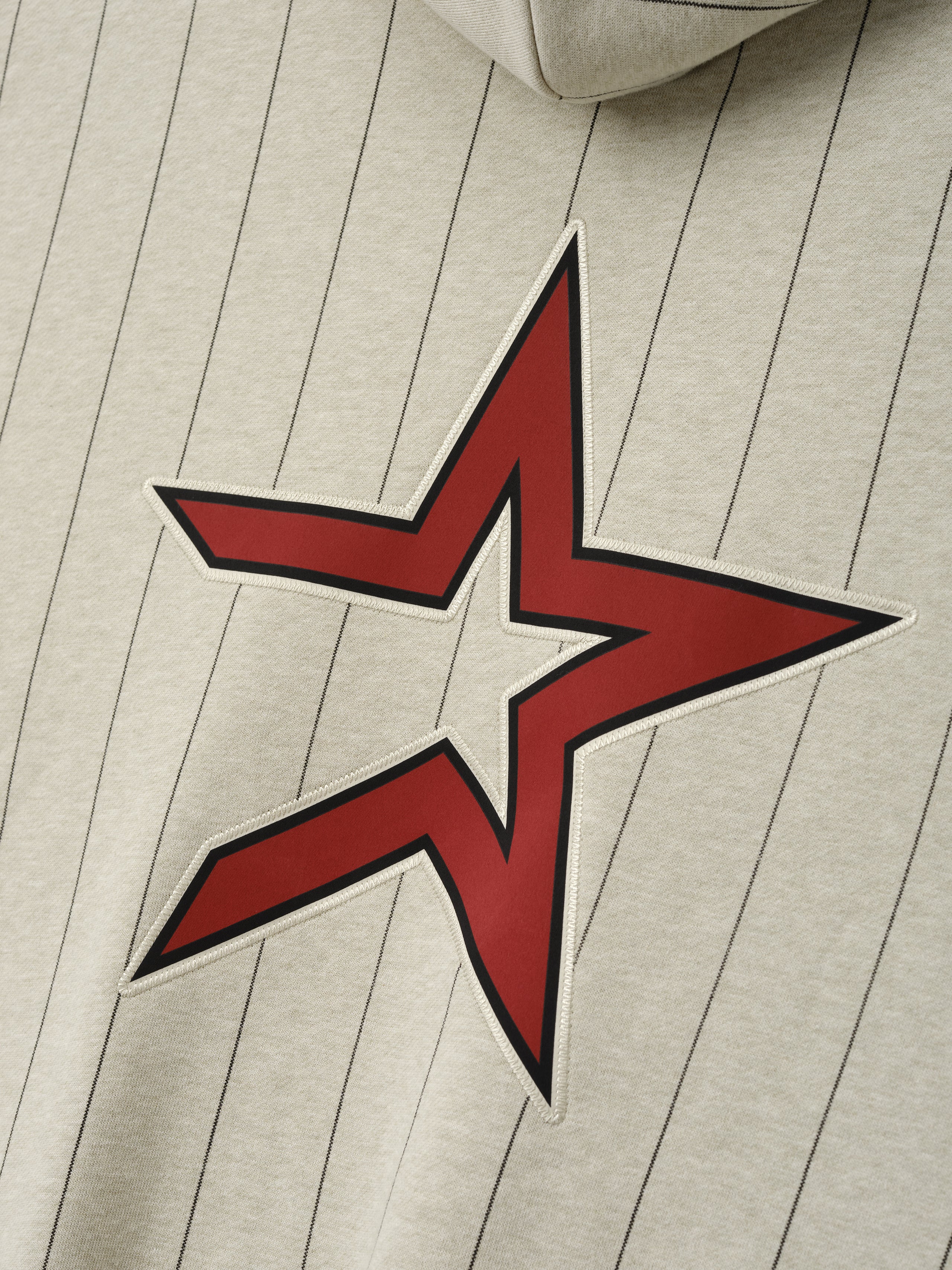 Close-up of Astros Sport Hoodie in a light stone shade with thin black pinstripes, featuring a large red star graphic with white outline on soft outerwear fabric.