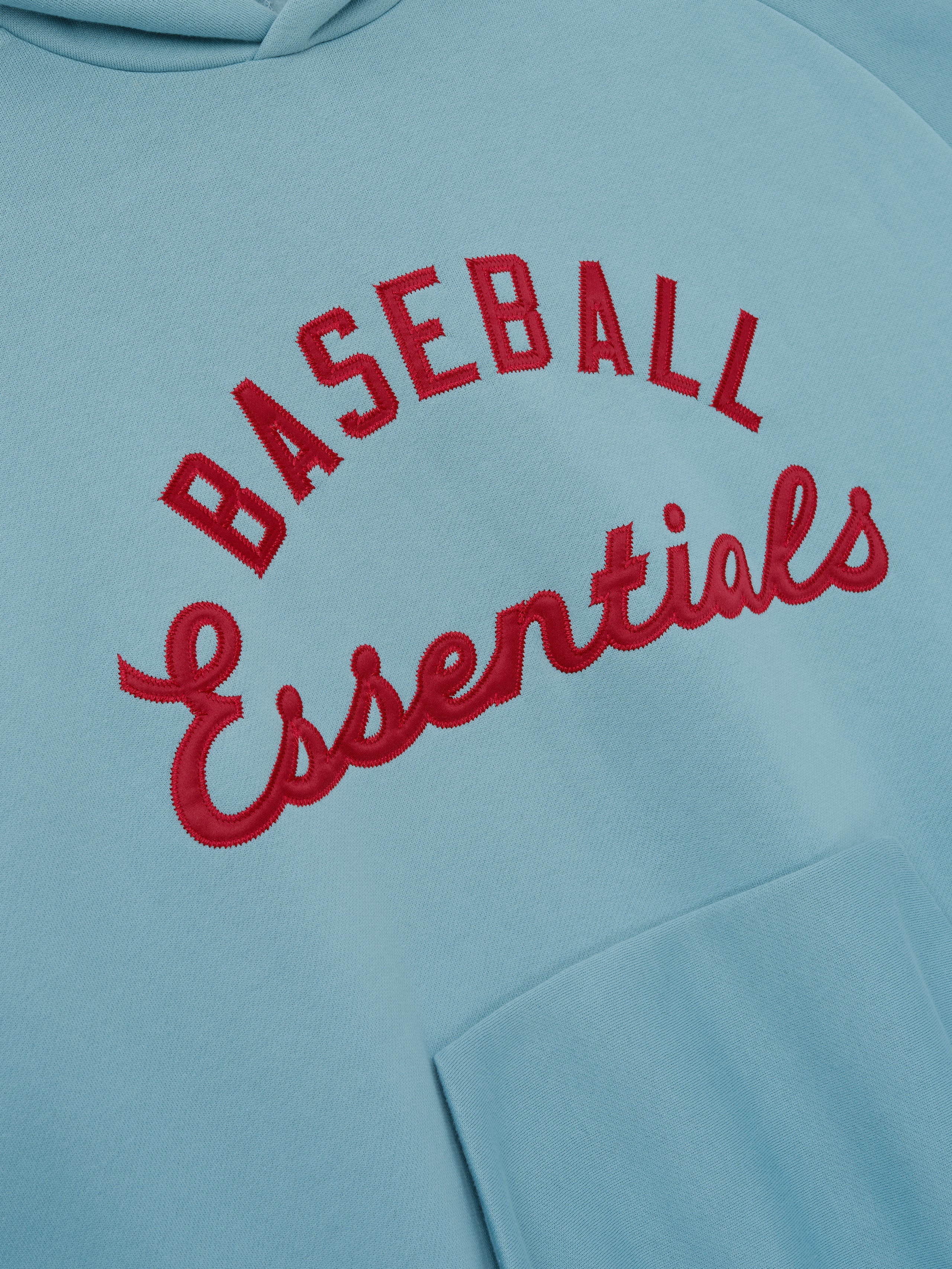 Close-up of a soft blue Mlb Raglan Sport Hoodie featuring raised red embroidered "Baseball Essentials" text on the front with a visible front kangaroo pocket, highlighting casual outerwear.