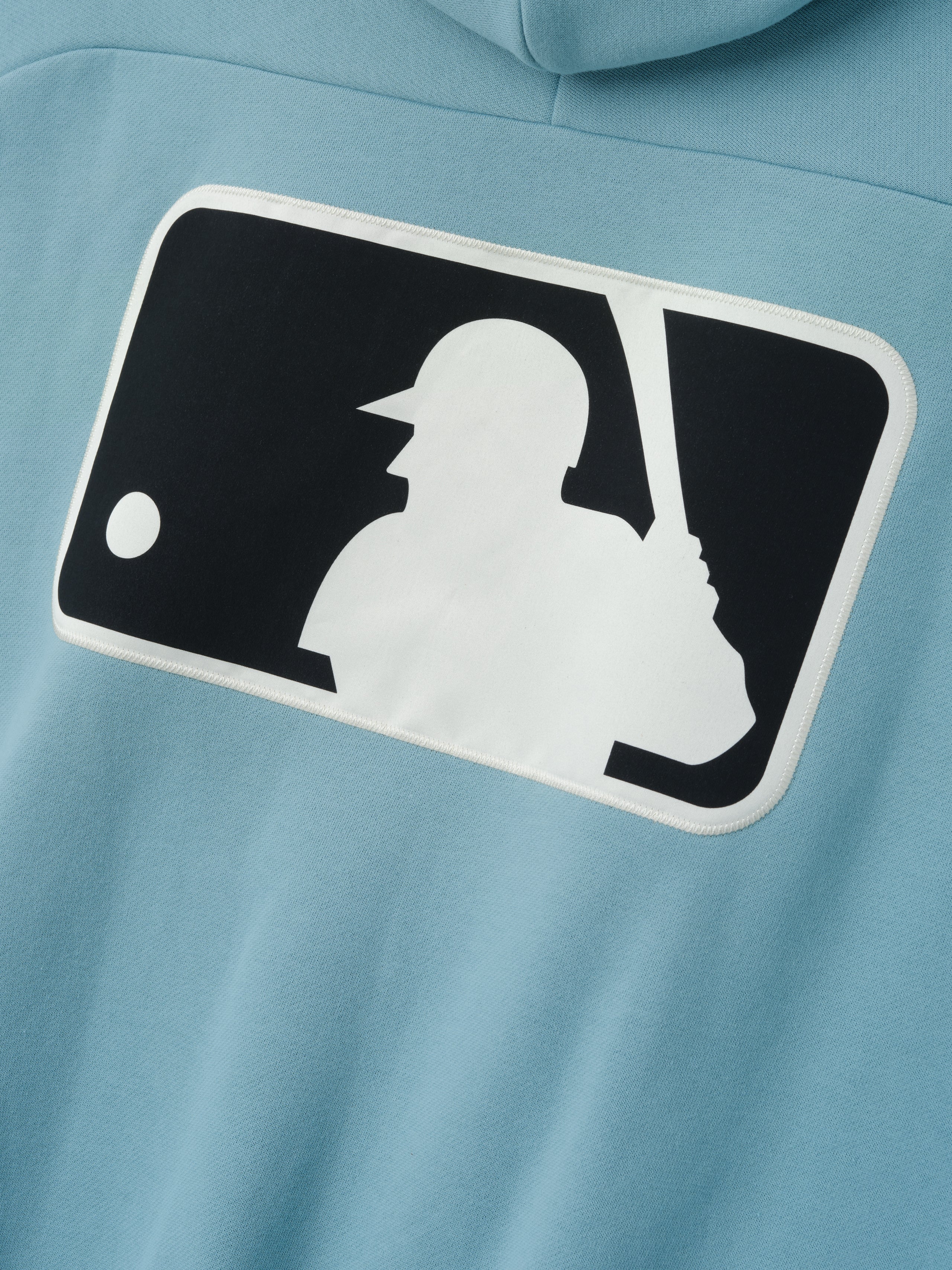 Close-up of the back of a pale blue Mlb Raglan Sport Hoodie featuring a large contrasting black and white graphic of a baseball batter, highlighting casual outerwear details.