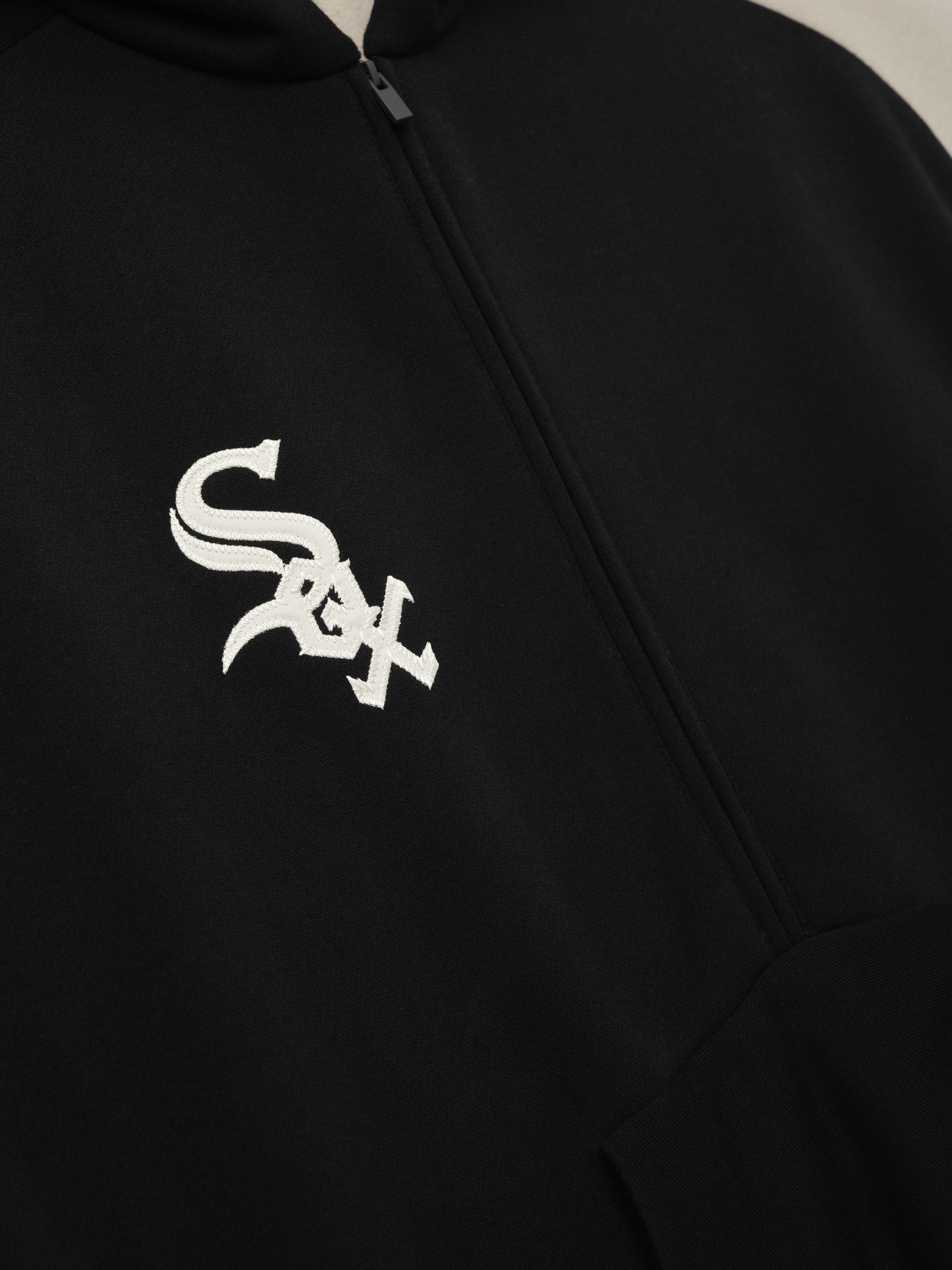 Close-up of the front of the White Sox Raglan Half Zip Sport Hoodie in black, featuring a white embroidered team logo above the kangaroo pocket and a minimalist quarter-zip closure.