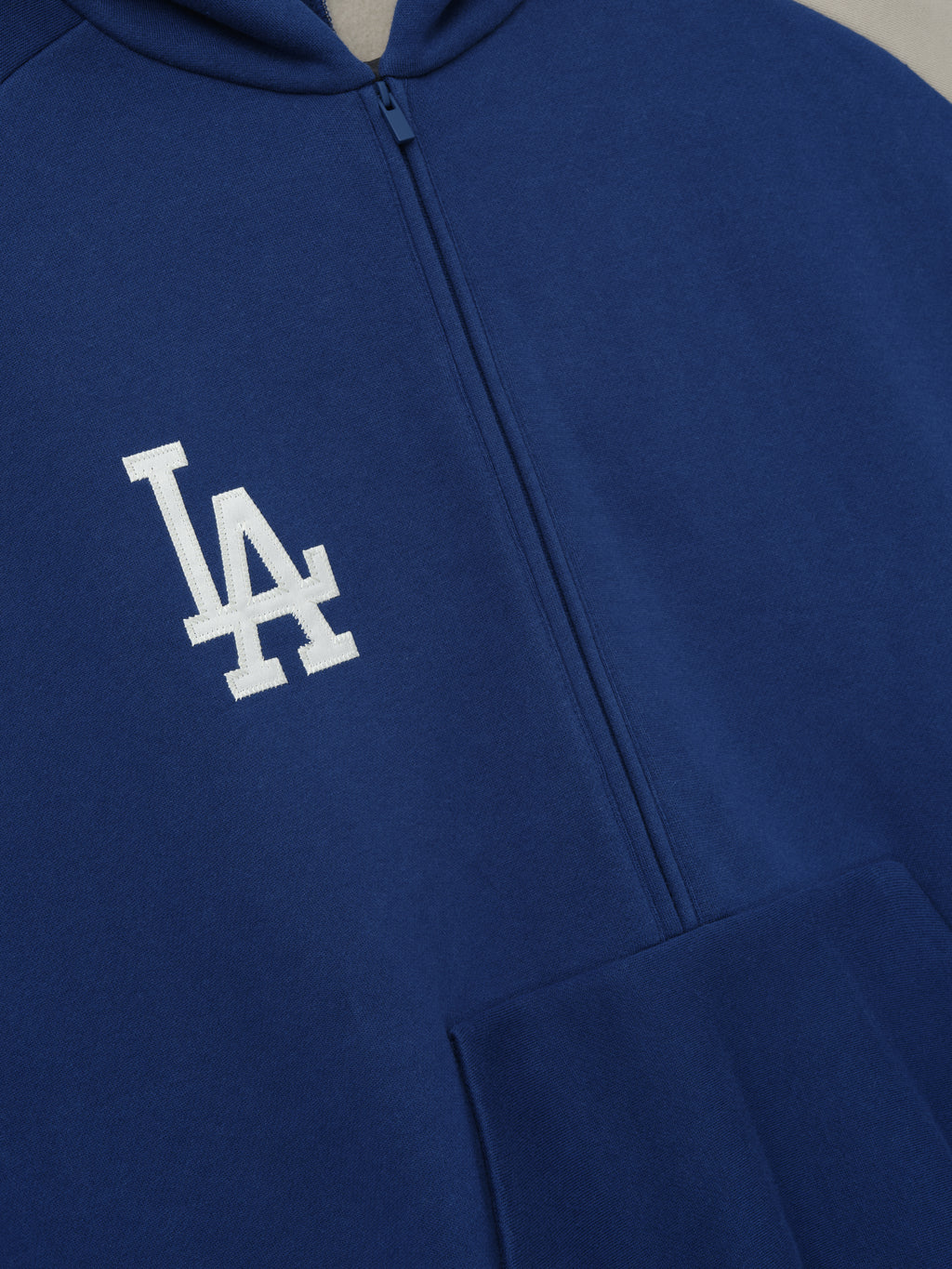 Close-up of Dodgers Raglan Half Zip Sport Hoodie in deep blue fabric featuring a white embroidered LA logo on the chest and a central zipper, styled as casual outerwear.