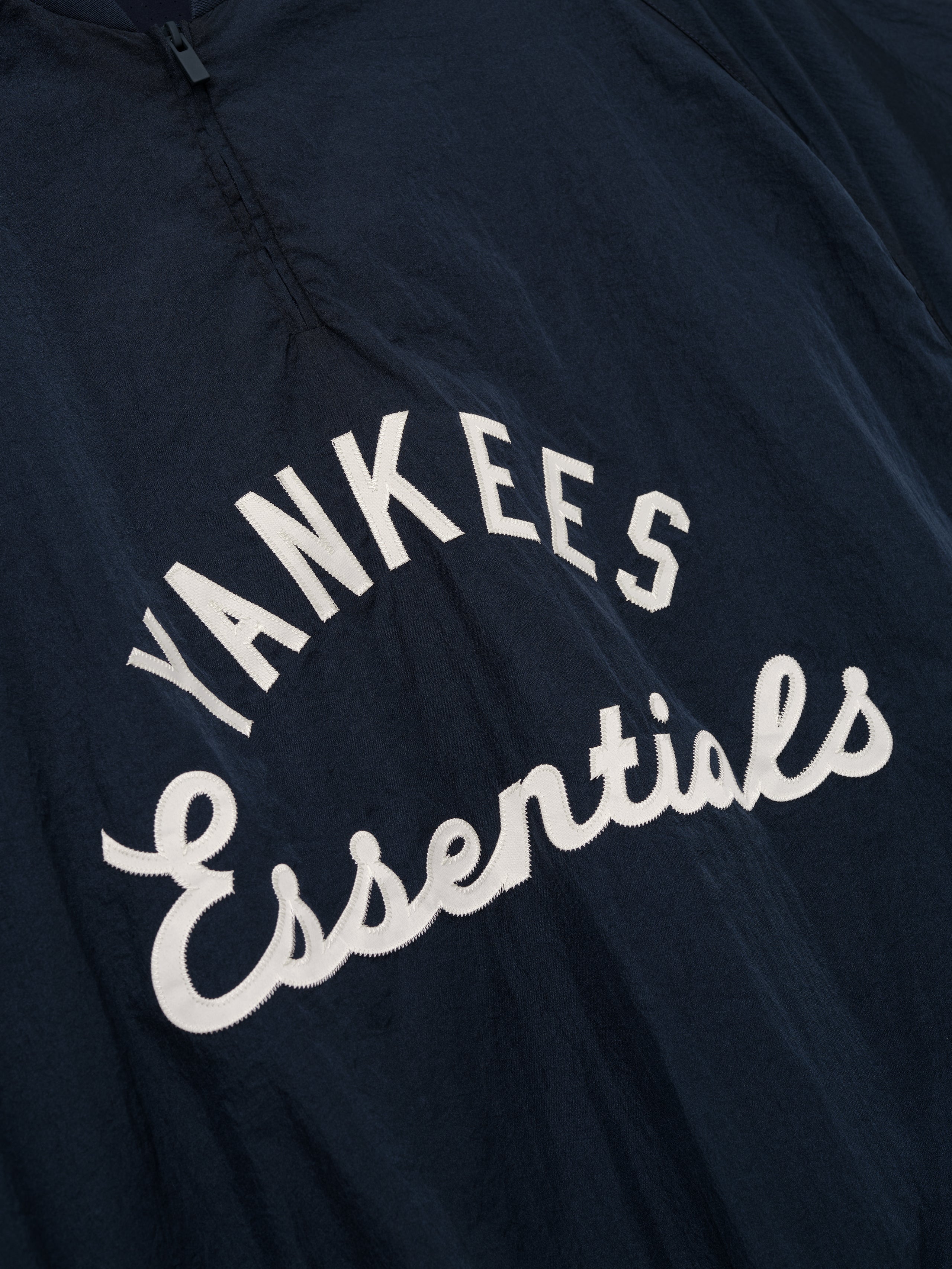 Close-up of a dark sapphire Yankees Half Zip Pullover featuring white embroidered "Yankees Essentials" text across the chest on a lightweight outerwear top.