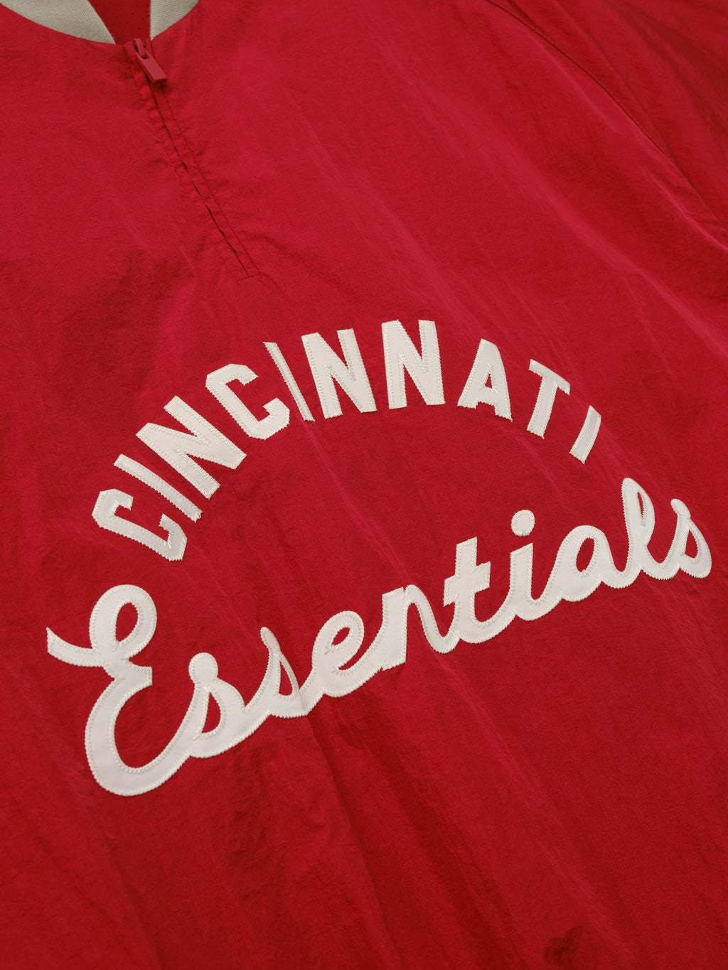 Reds Half Zip Pullover in a vibrant red fabric featuring textured white "Cincinnati Essentials" lettering across the front, designed as a lightweight outerwear top with a half zipper.