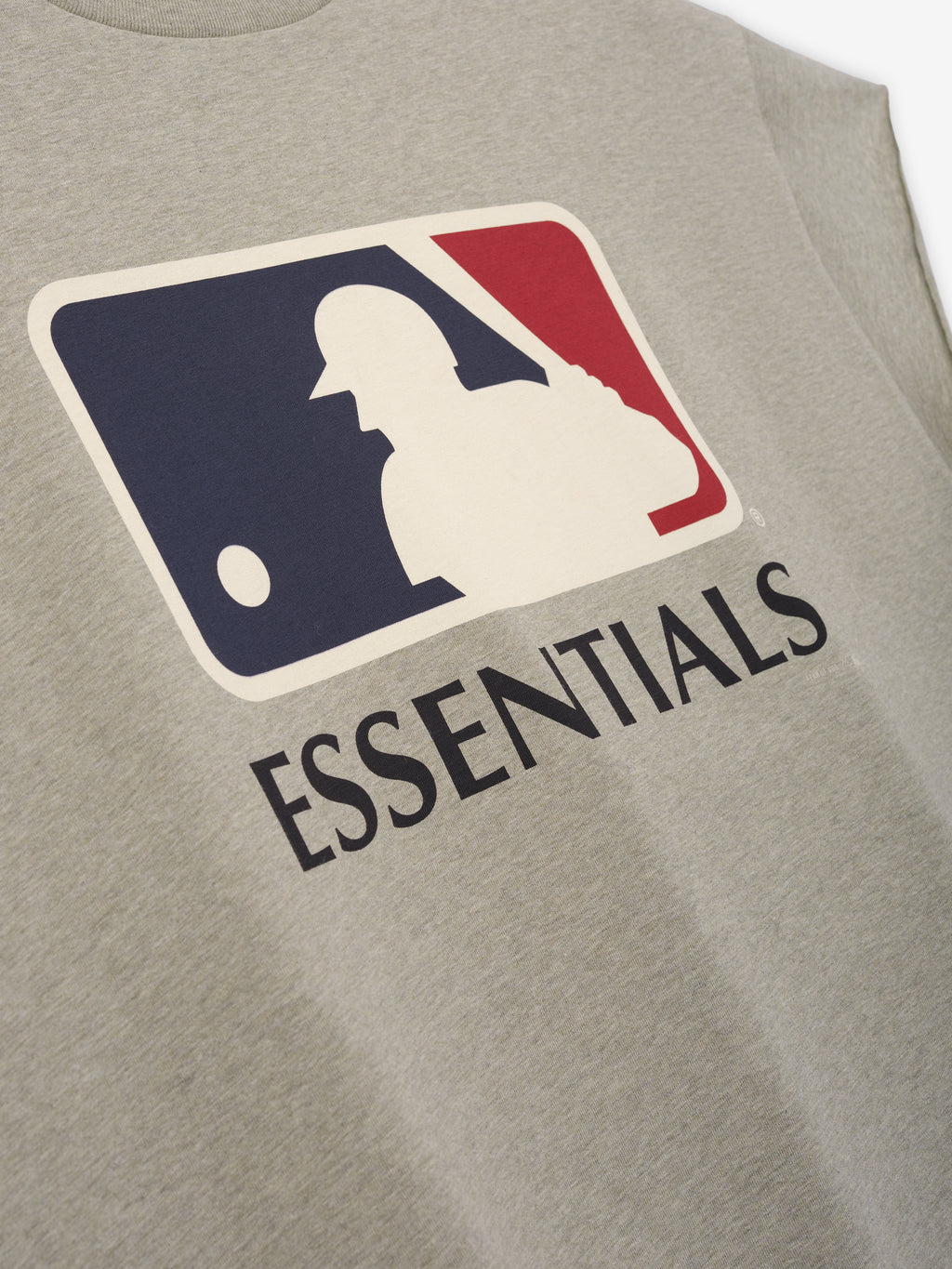 Close-up of a soft heather gray fabric on the Fear Of God X Franklin 90s Cutoff featuring a vintage-style baseball player silhouette in navy and red above bold "ESSENTIALS" text.