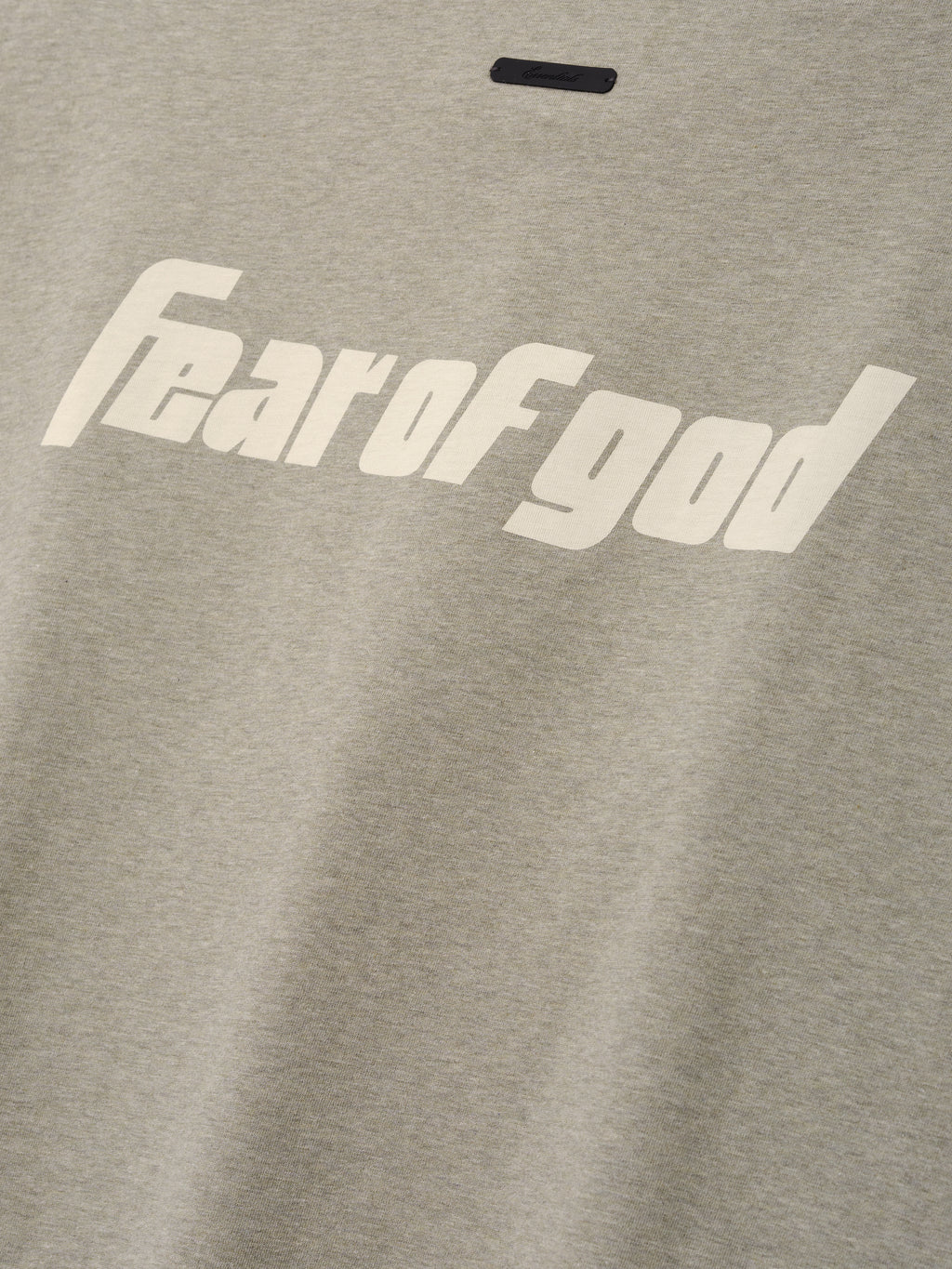 Close-up of light gray fabric on the Fear Of God X Franklin 90s Cutoff featuring bold cream "fear of god" text printed across the soft textile top.