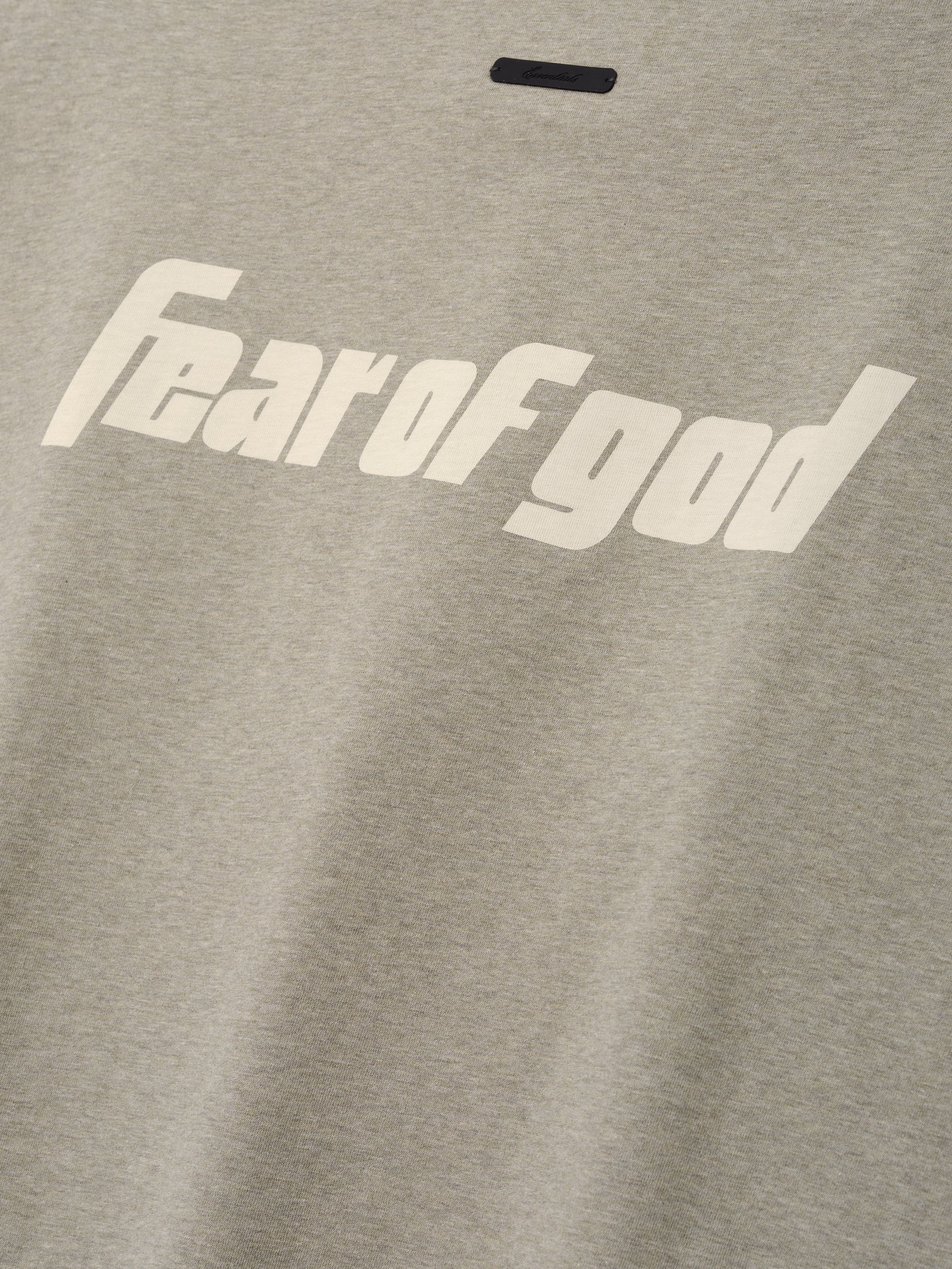 Close-up of light gray fabric on the Fear Of God X Franklin 90s Cutoff featuring bold cream "fear of god" text printed across the soft textile top.