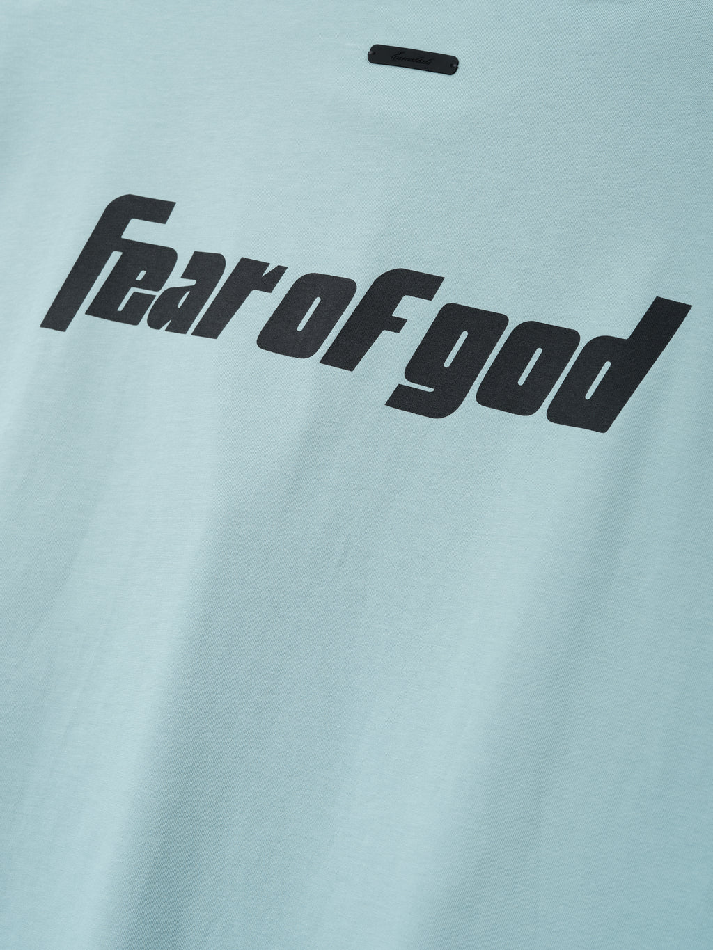 Close-up of a soft stone blue fabric from the Fear Of God X Franklin 90s Cutoff featuring bold black "fear of god" text printed across the smooth textile surface.
