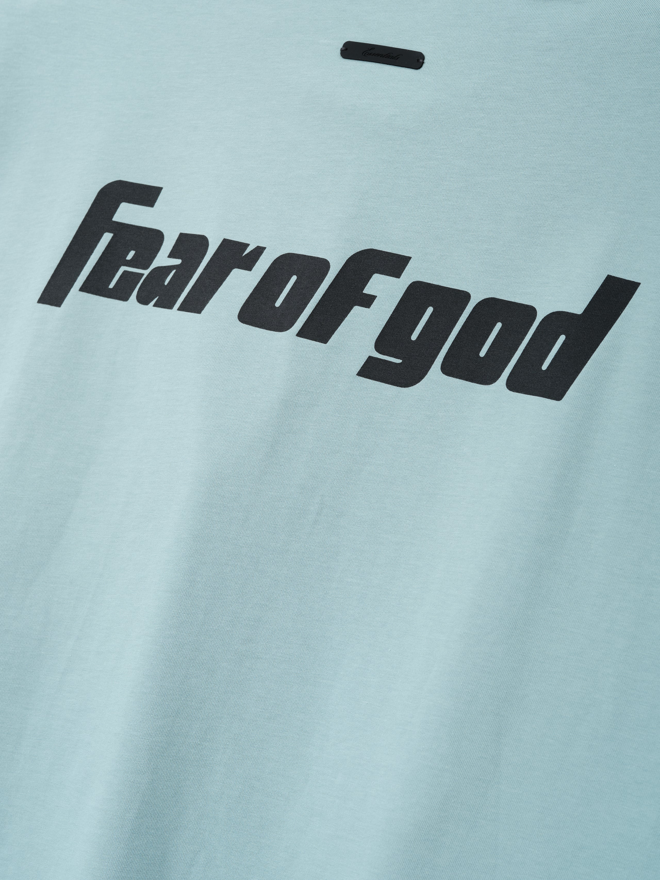 Close-up of a soft stone blue fabric from the Fear Of God X Franklin 90s Cutoff featuring bold black "fear of god" text printed across the smooth textile surface.