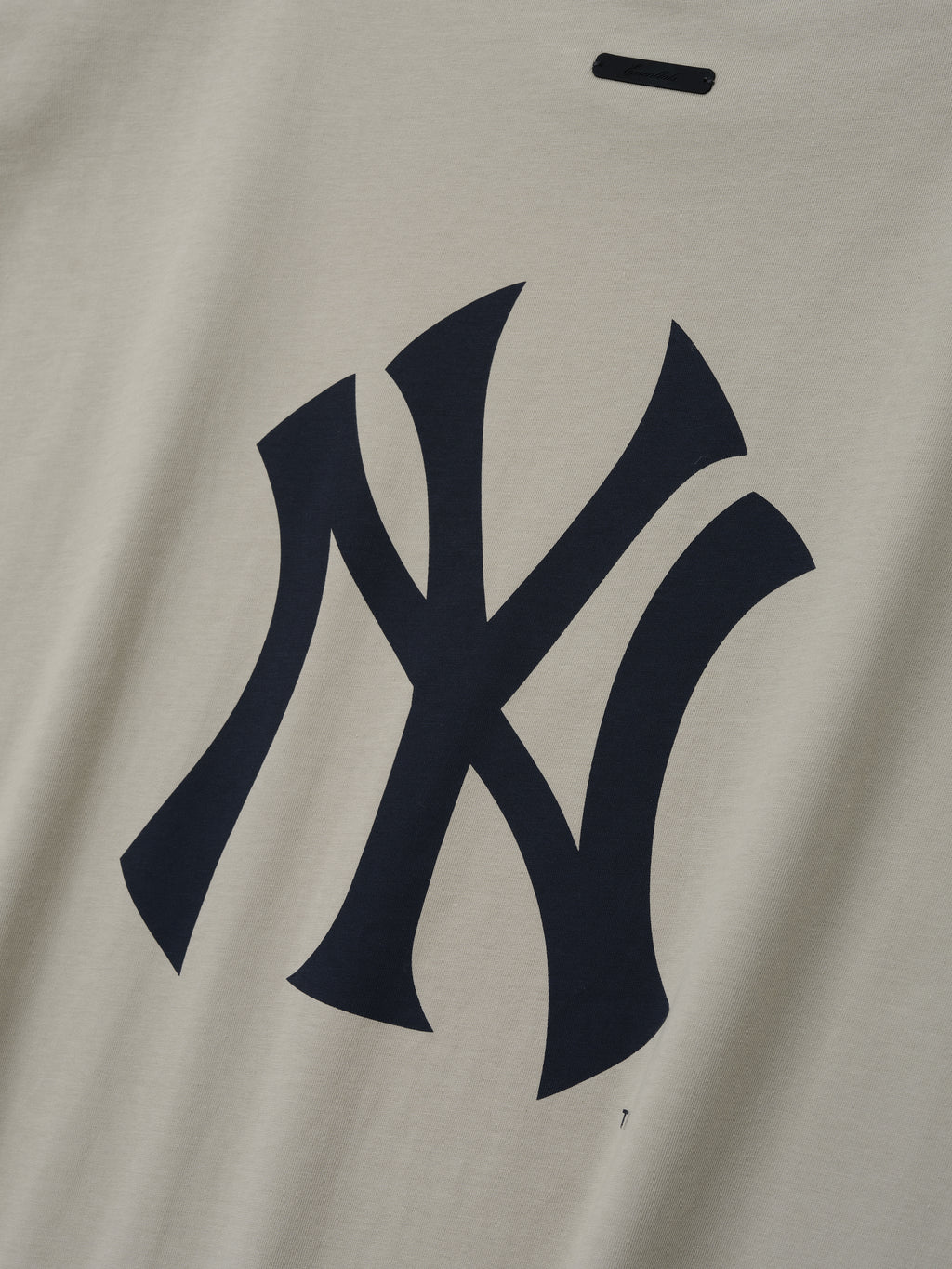 Yankees 90s Cut Off featuring a bold navy Yankees logo printed on soft beige cotton fabric, highlighting a vintage-inspired design for a casual, timeless look.