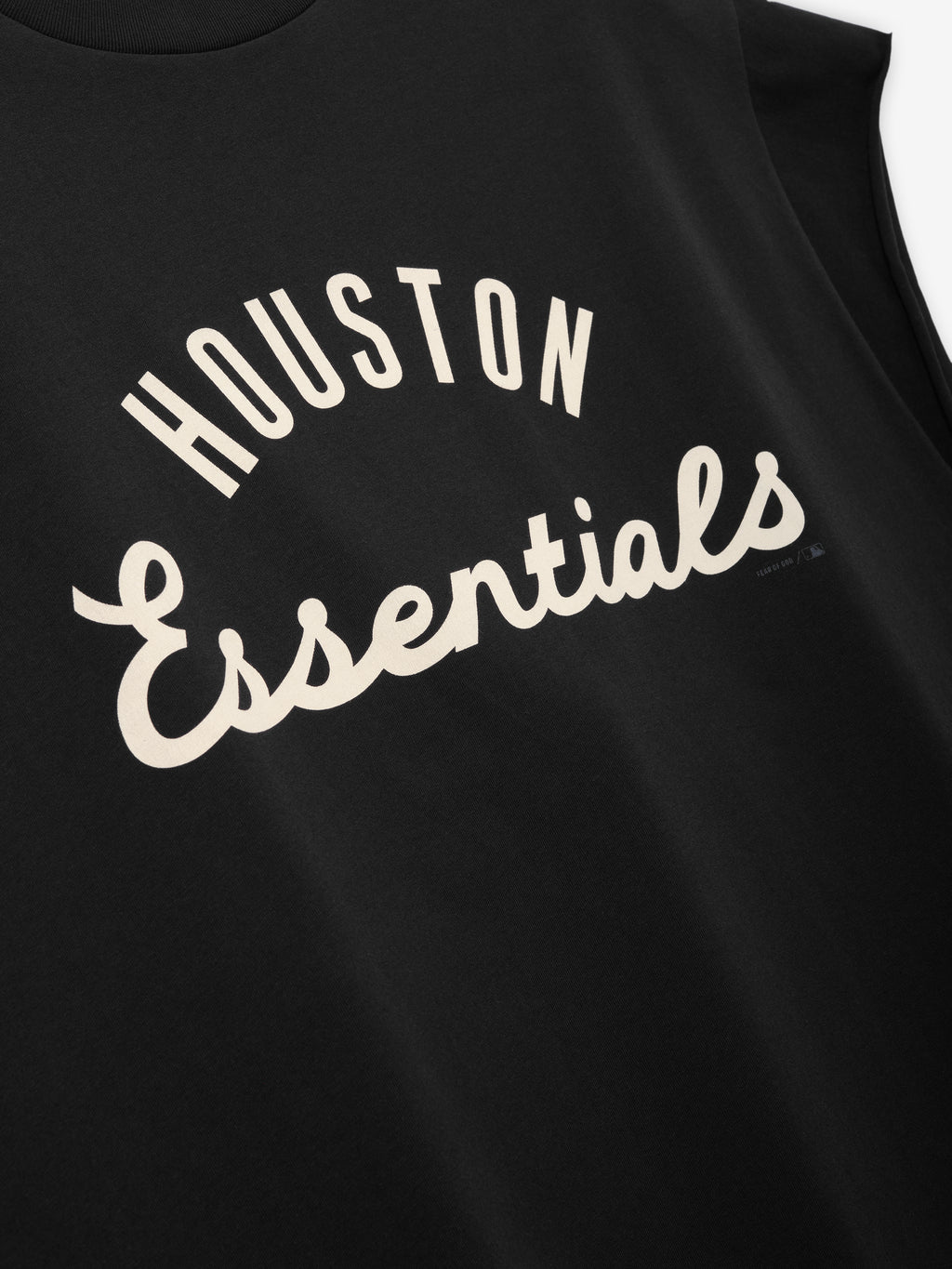 Close-up of a black sleeveless top displaying cream-colored text "Houston Essentials" in a curved design on the front, part of the Astros 90s Cut Off collection.