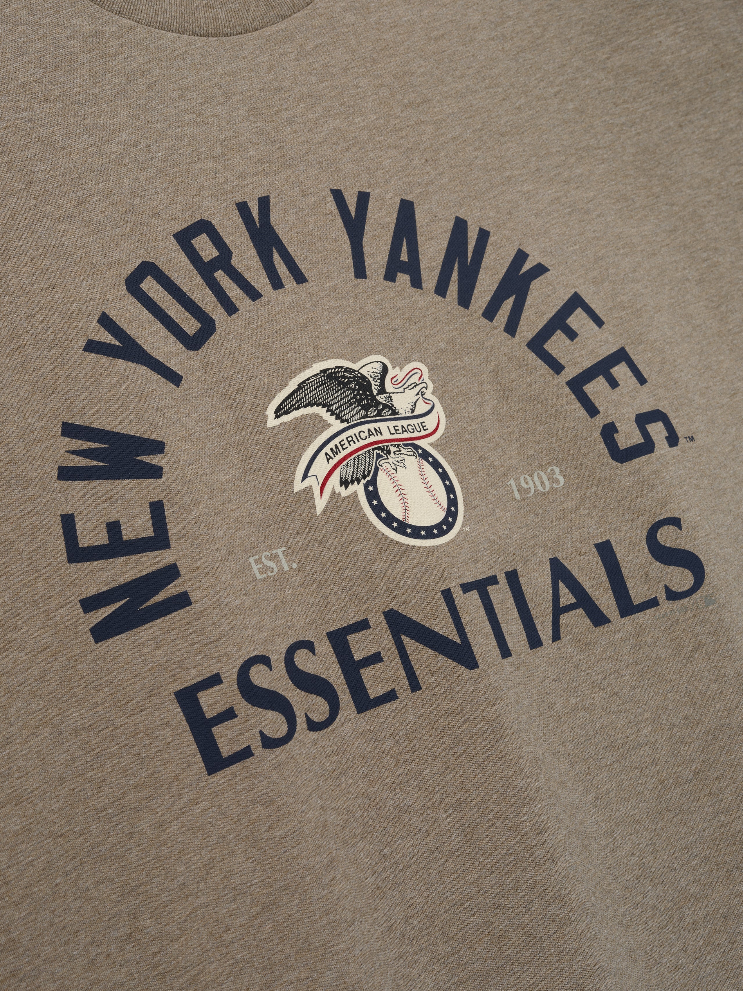 Yankees AL Merch Tee in soft brown heather fabric featuring bold navy "New York Yankees Essentials" text and a vintage American League eagle graphic on a casual top.