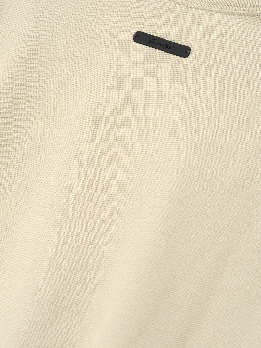 Close-up of a sandstone-colored fabric with a small rectangular black tag sewn near the neckline, part of the Astros Al Merch Tee collection.