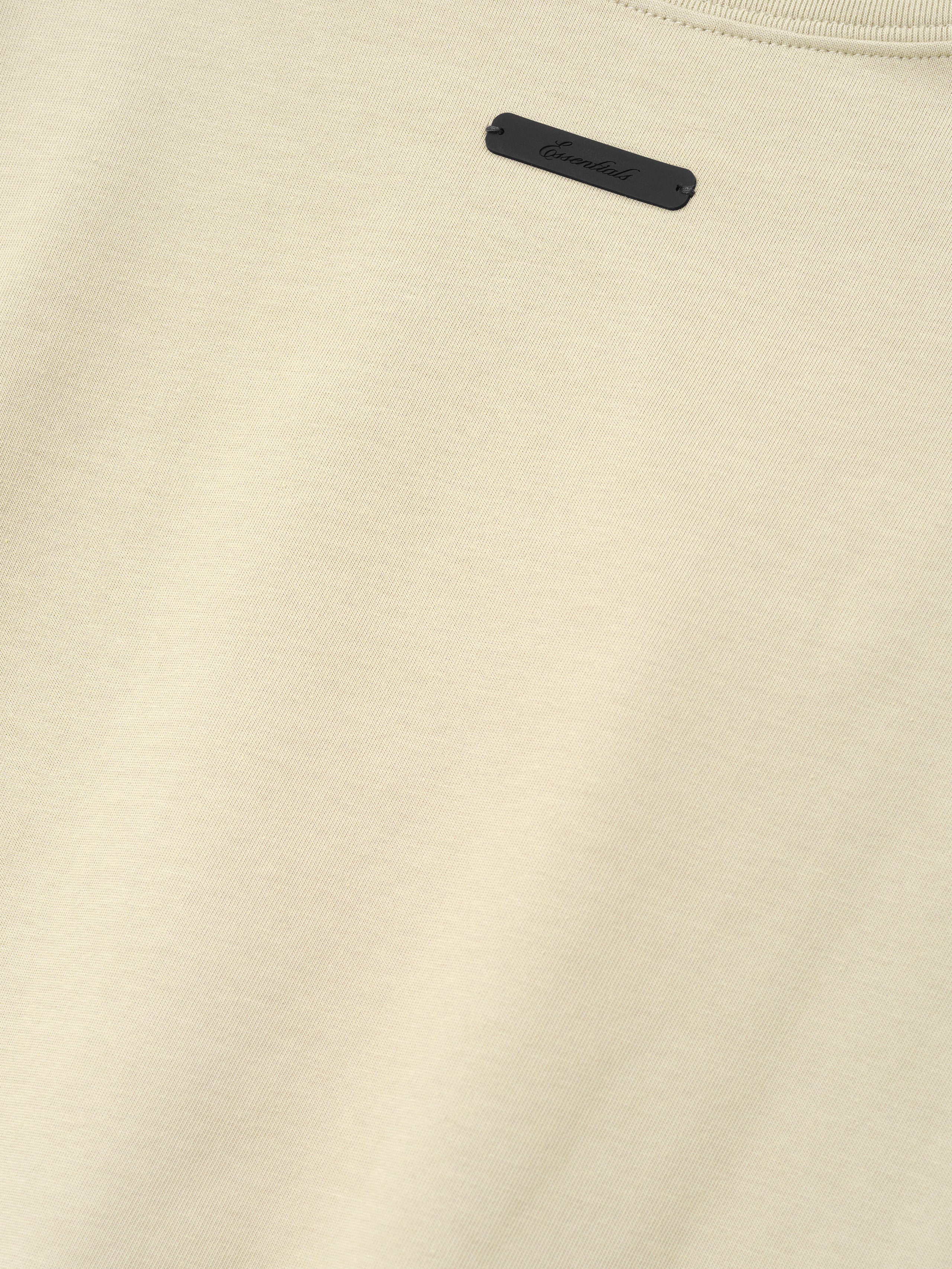 Close-up of a sandstone-colored fabric with a small rectangular black tag sewn near the neckline, part of the Astros Al Merch Tee collection.