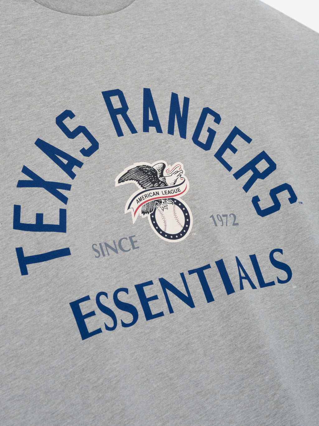 Rangers AL Merch Tee in a soft concrete heather fabric featuring bold navy "Texas Rangers Essentials" text with a vintage eagle and baseball graphic at the center.