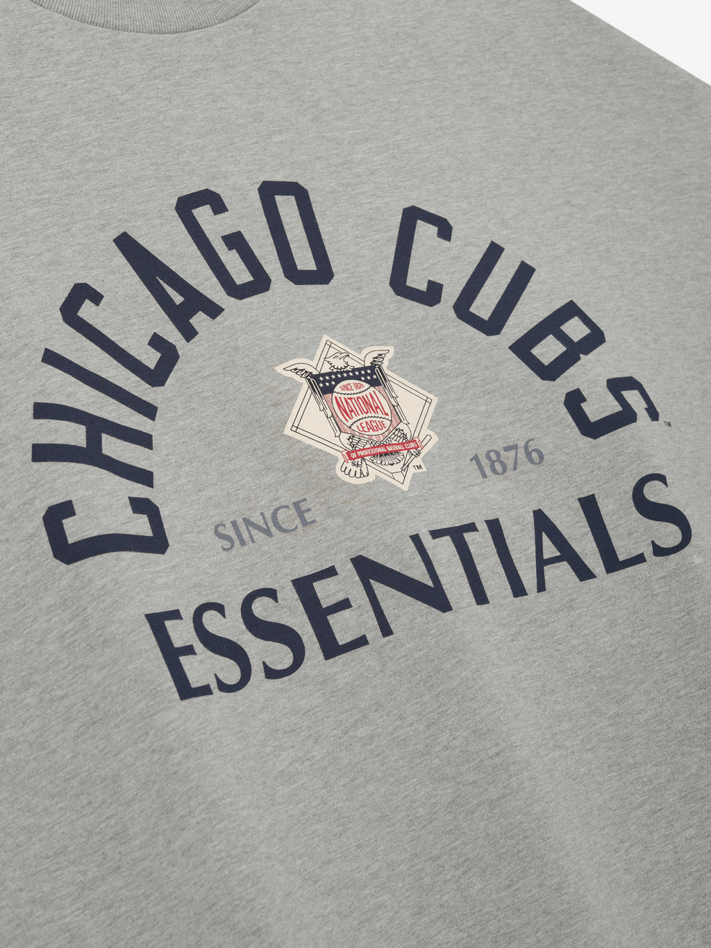 Close-up of a light grey Cubs NL Merch Tee featuring navy blue "Chicago Cubs Essentials" text arched above and below a vintage emblem with "Since 1876" detail on soft fabric.