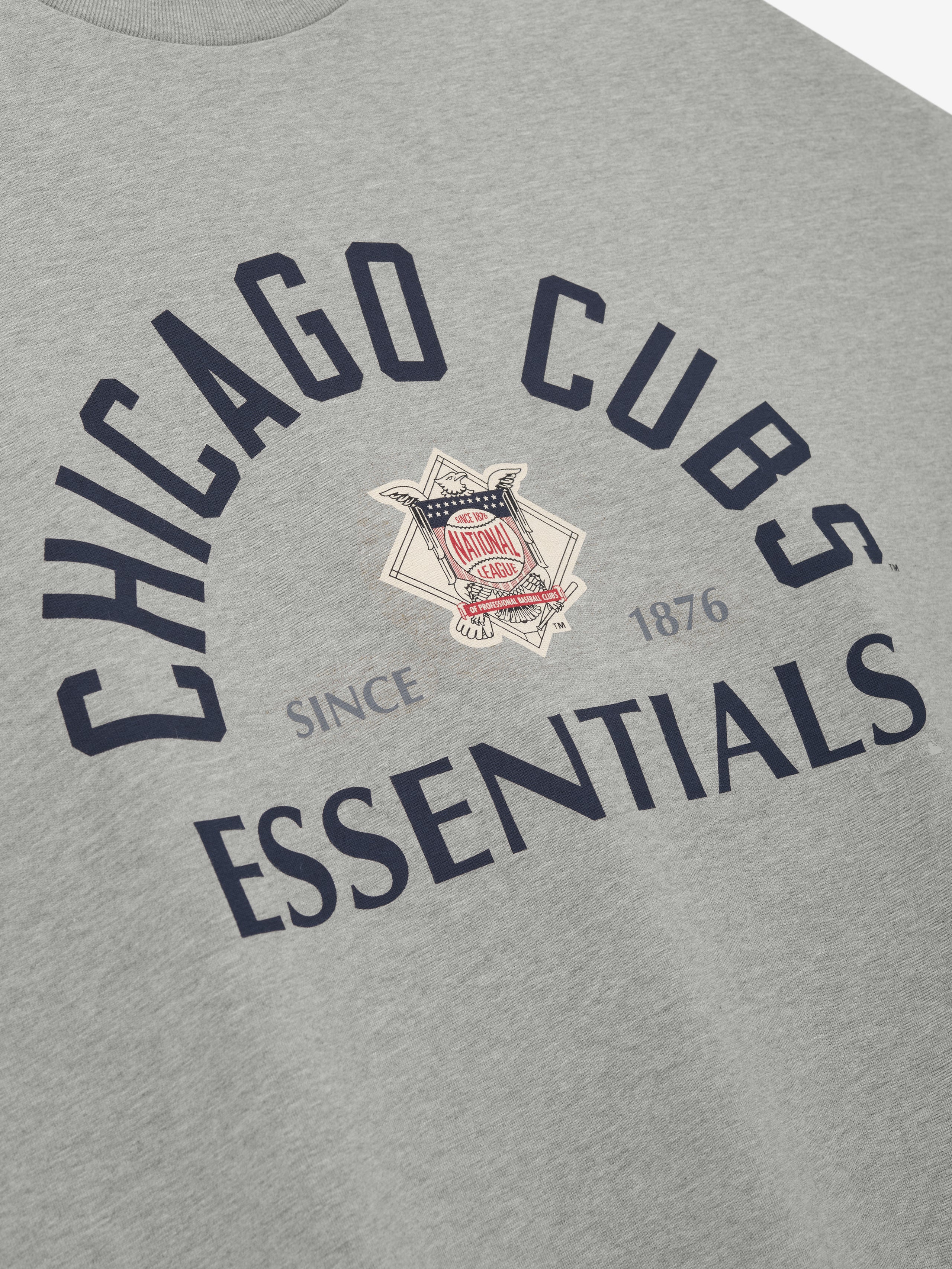 Close-up of a light grey Cubs NL Merch Tee featuring navy blue "Chicago Cubs Essentials" text arched above and below a vintage emblem with "Since 1876" detail on soft fabric.