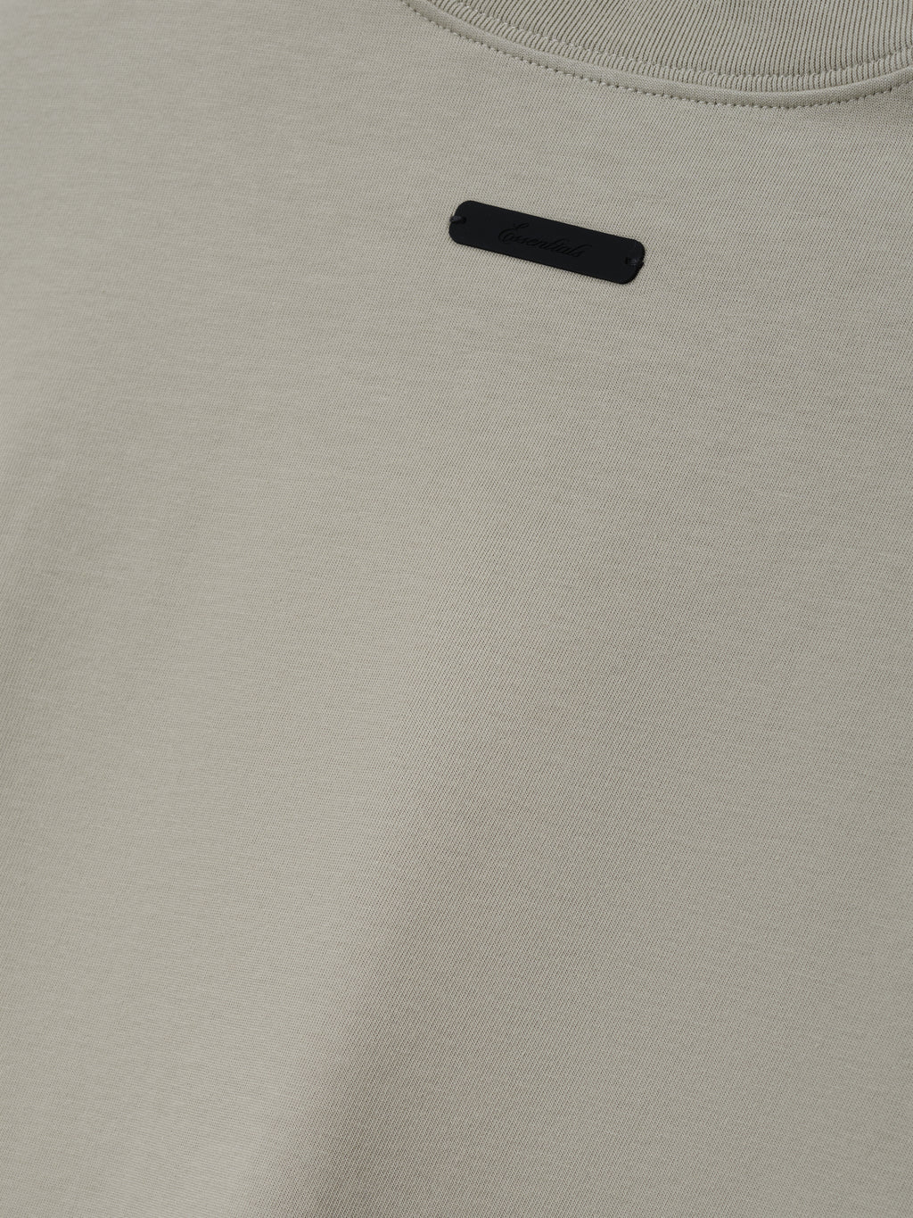Reds NL Merch Tee in a soft neutral beige shade featuring a minimalist design with a small black rectangular label near the neckline on smooth fabric.