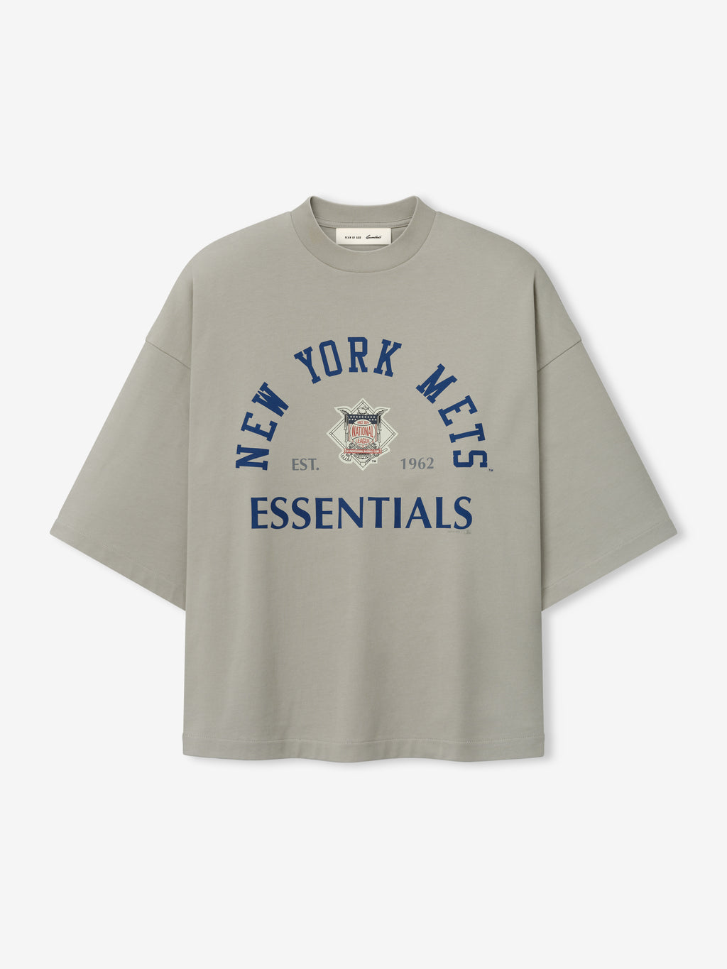 Front view of the Mets NL Merch Tee in muted gray featuring navy blue "New York Mets" text arched above a vintage team logo and bold "ESSENTIALS" text on soft fabric.