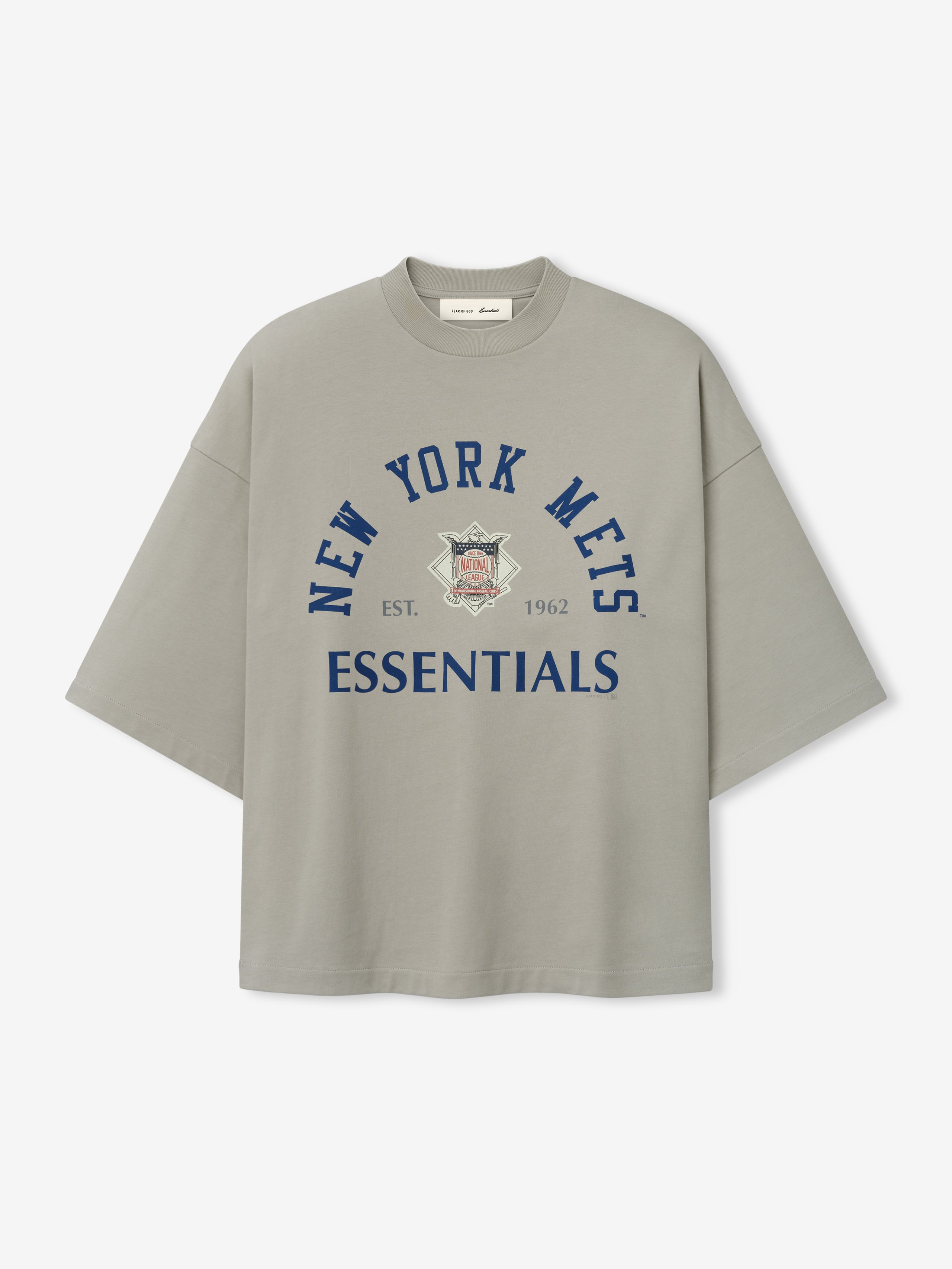 Front view of the Mets NL Merch Tee in muted gray featuring navy blue "New York Mets" text arched above a vintage team logo and bold "ESSENTIALS" text on soft fabric.