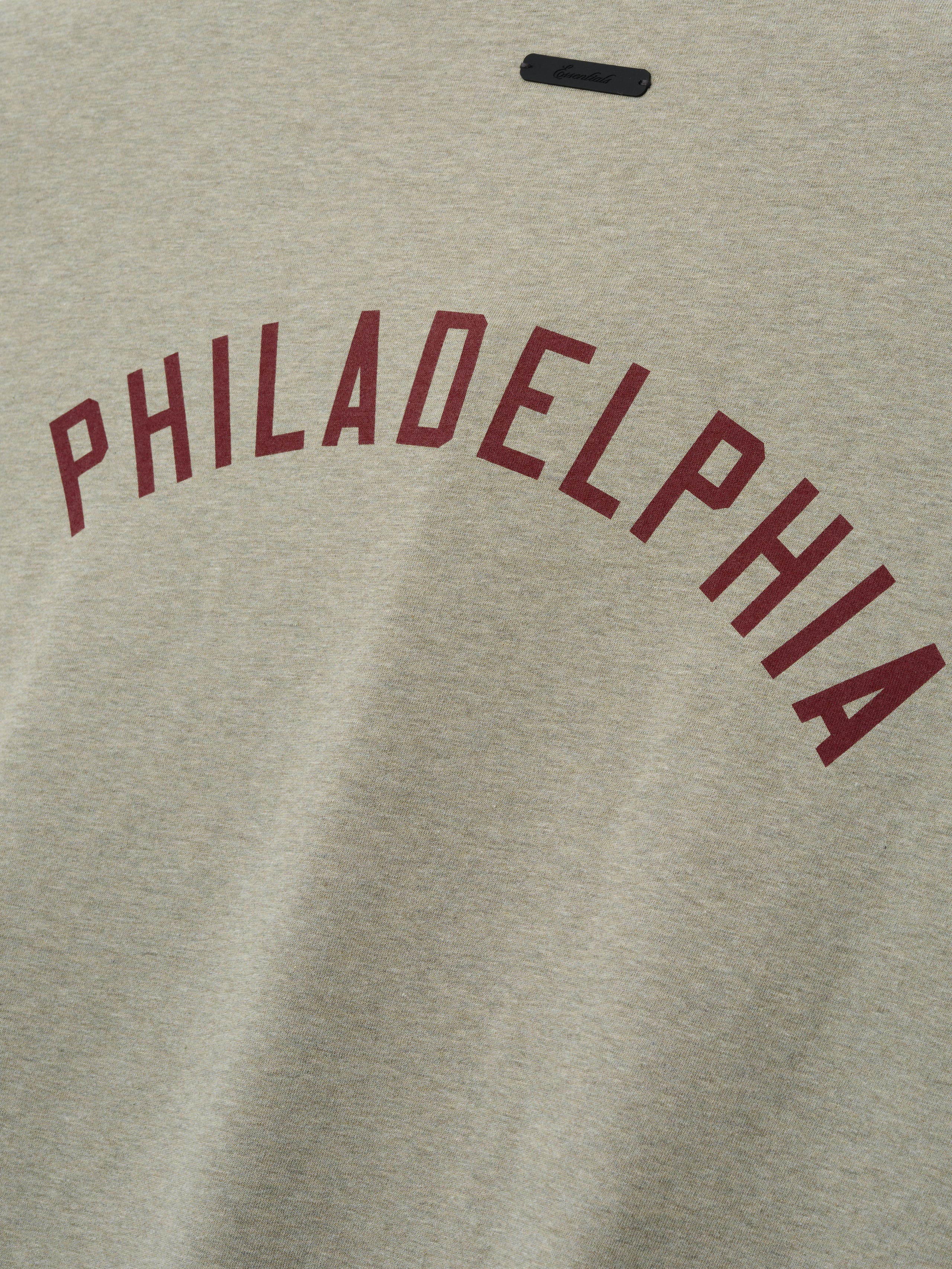 Phillies Merch Tee in a heathered light beige fabric featuring bold maroon "PHILADELPHIA" text arched across the chest, designed for a casual and comfortable fit.