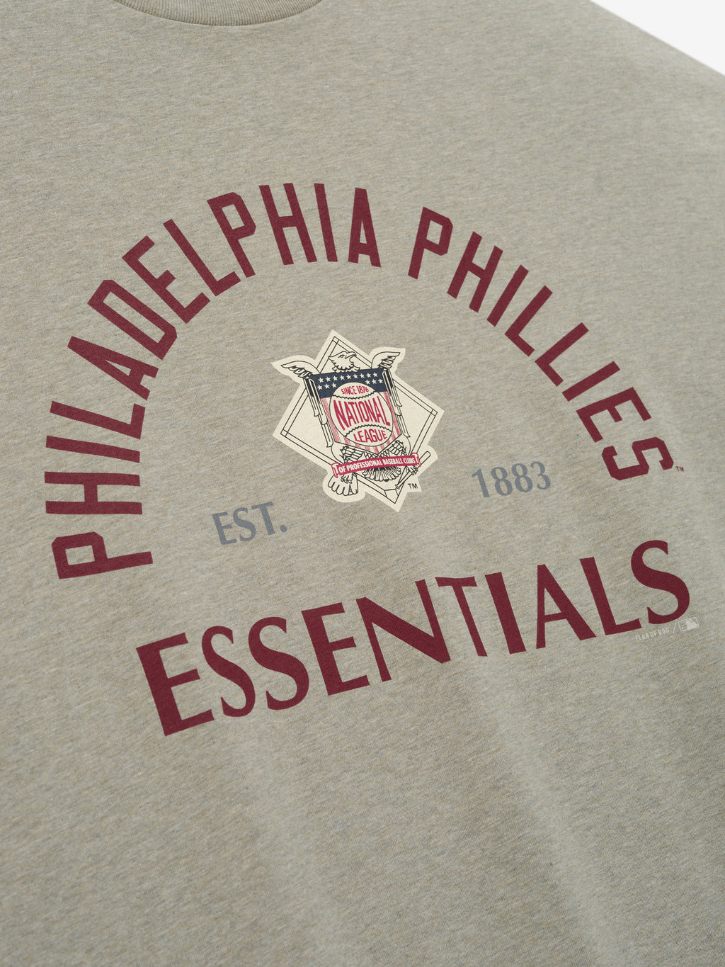 Phillies NL Merch Tee in a soft seal heather fabric with curved maroon "Philadelphia Phillies Essentials" text and a vintage National League emblem at the center, designed for casual wear.