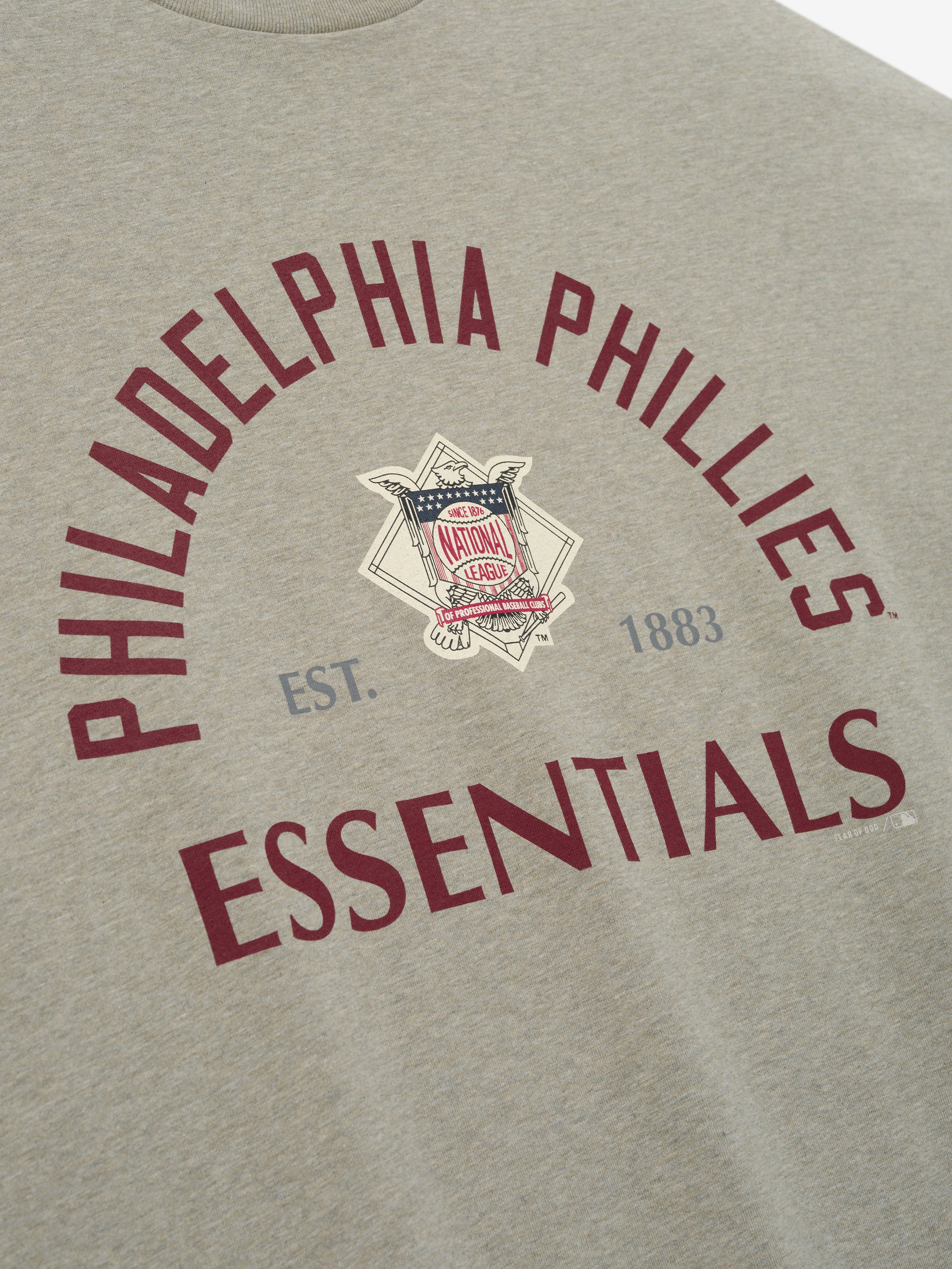 Phillies NL Merch Tee in a soft seal heather fabric with curved maroon "Philadelphia Phillies Essentials" text and a vintage National League emblem at the center, designed for casual wear.