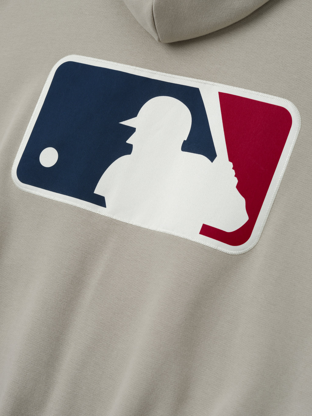 Close-up of a muted beige Mlb Full Zip Sport Hoodie showing a large sewn MLB logo patch in navy, white, and red on the back, emphasizing detailed stitching and texture.