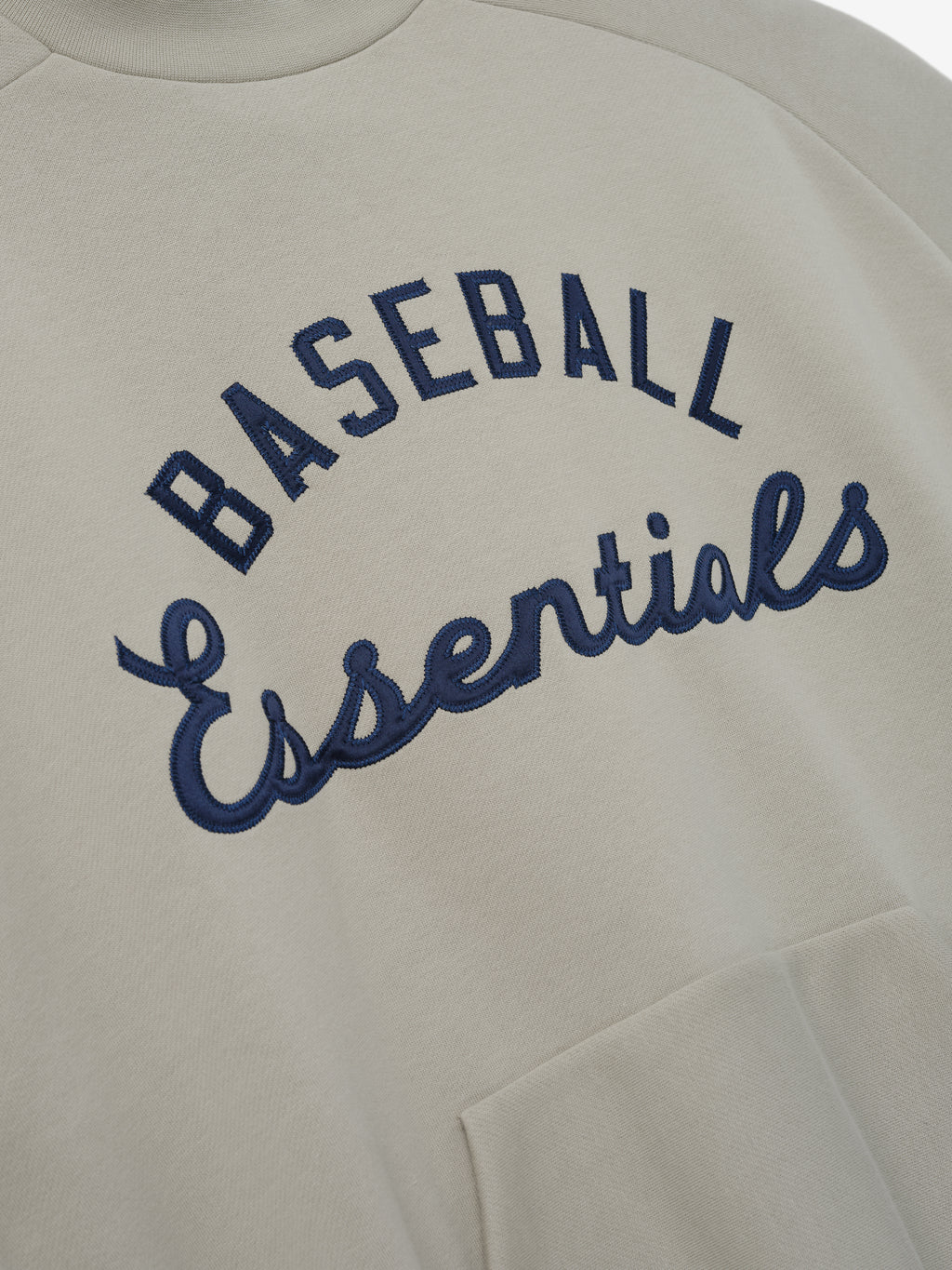 Mlb Sport Crewneck in a muted beige tone featuring navy blue embroidered "Baseball Essentials" text arching across the chest with a soft fabric and a front kangaroo pocket for casual layering.