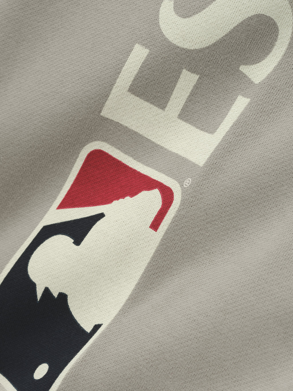 Close-up view of a muted gray Mlb Lounge Sweatpant fabric featuring a bold vertical logo with red, black, and cream graphic elements on casual bottoms.