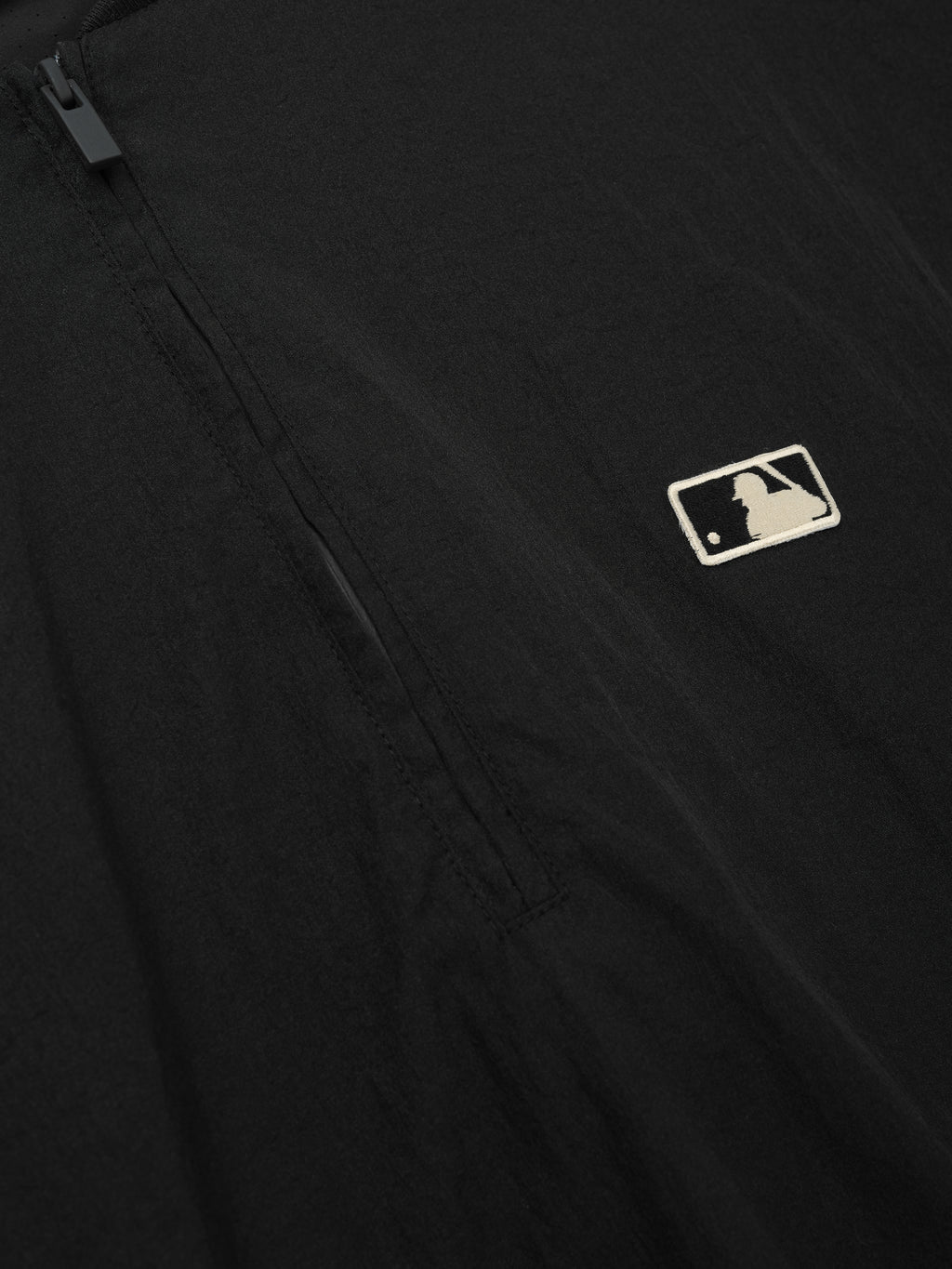 Close-up of a black Mlb 3/4 Sleeve Pullover highlighting a subtle embroidered logo near a sleek quarter-zip closure on smooth fabric, emphasizing minimalist design in a top layer.