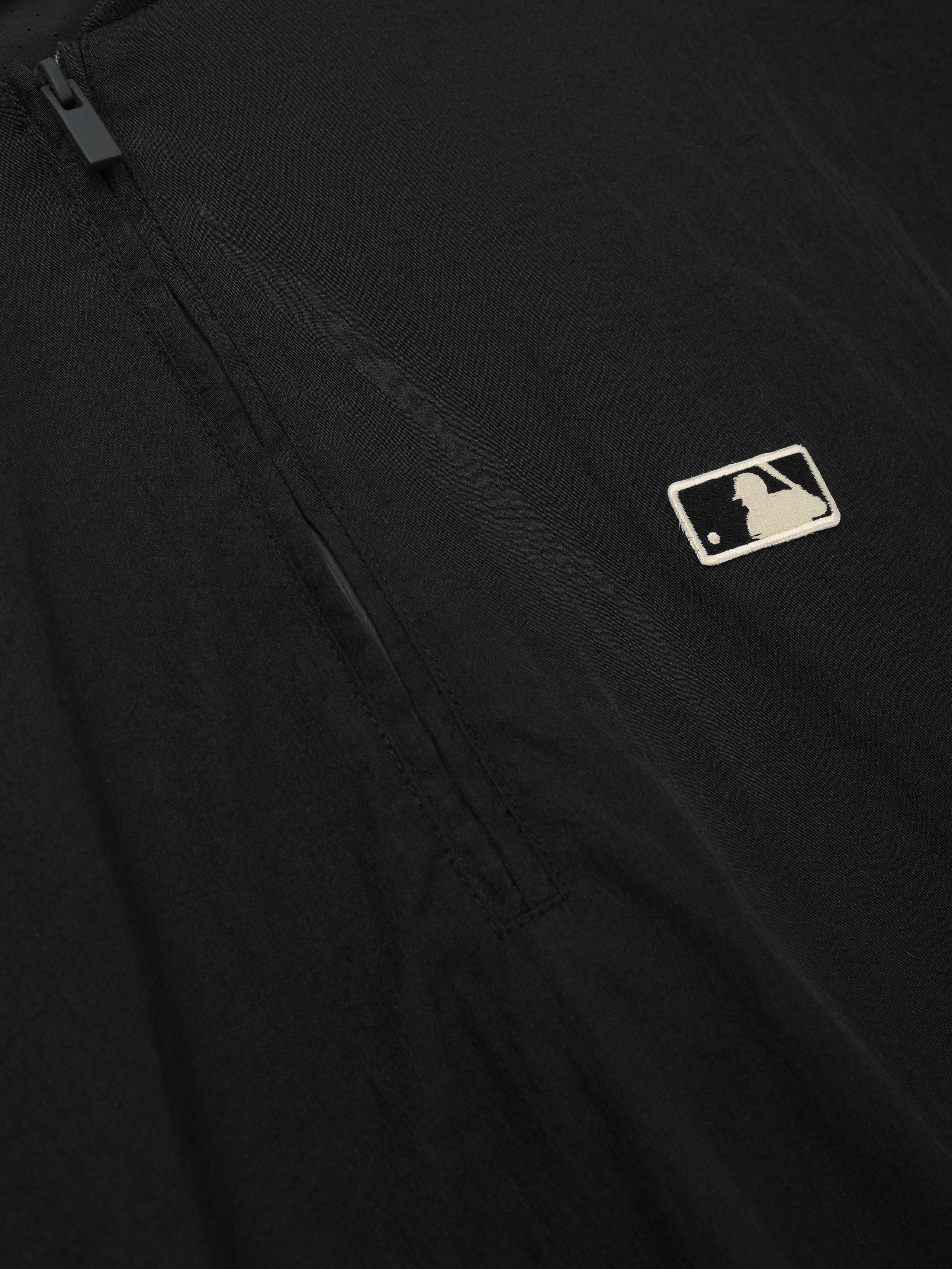 Close-up of a black Mlb 3/4 Sleeve Pullover highlighting a subtle embroidered logo near a sleek quarter-zip closure on smooth fabric, emphasizing minimalist design in a top layer.