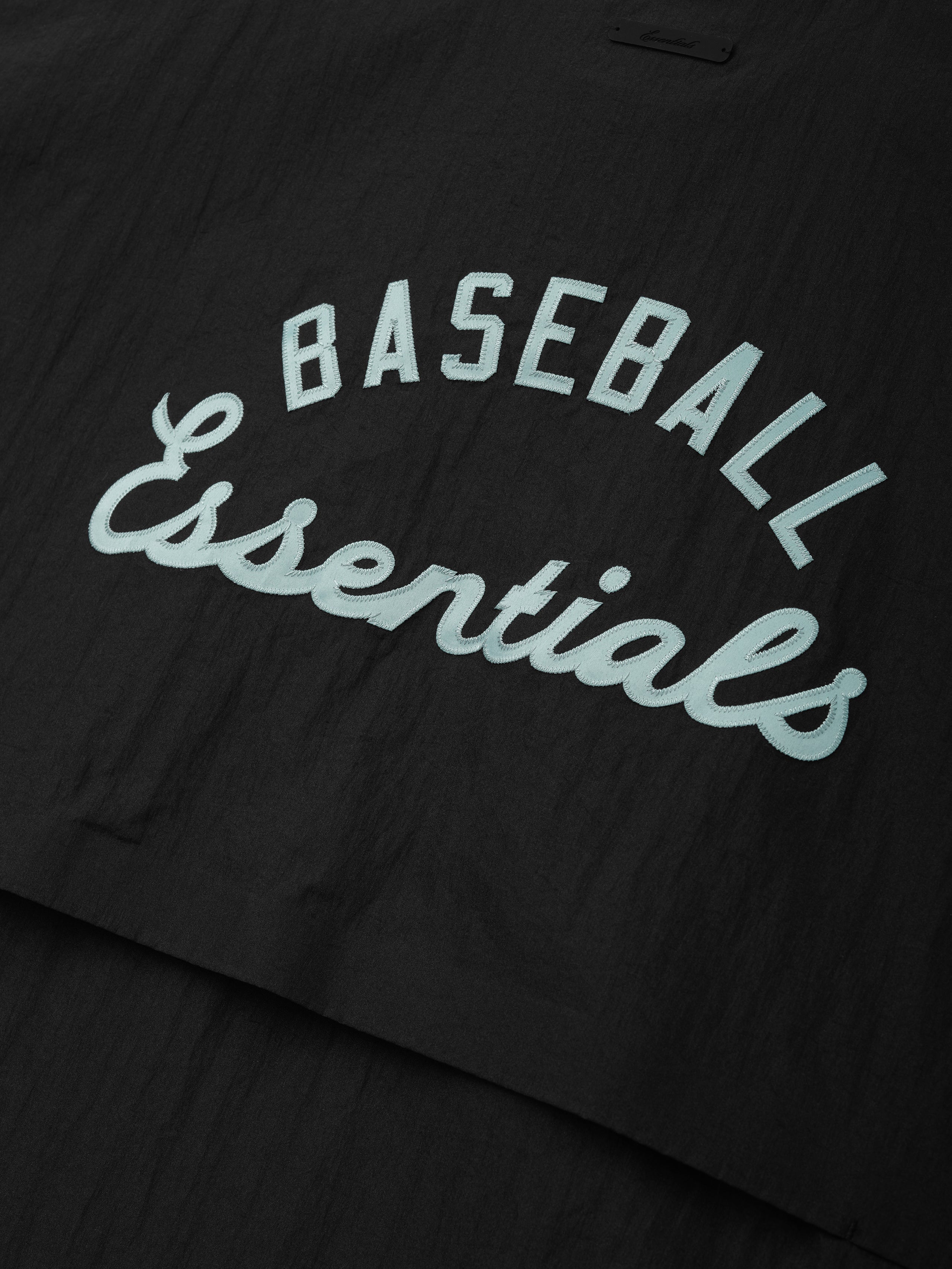 Close-up of black fabric from the Mlb 3/4 Sleeve Pullover featuring raised light blue "BASEBALL Essentials" text in contrasting fonts on a smooth, lightweight material.