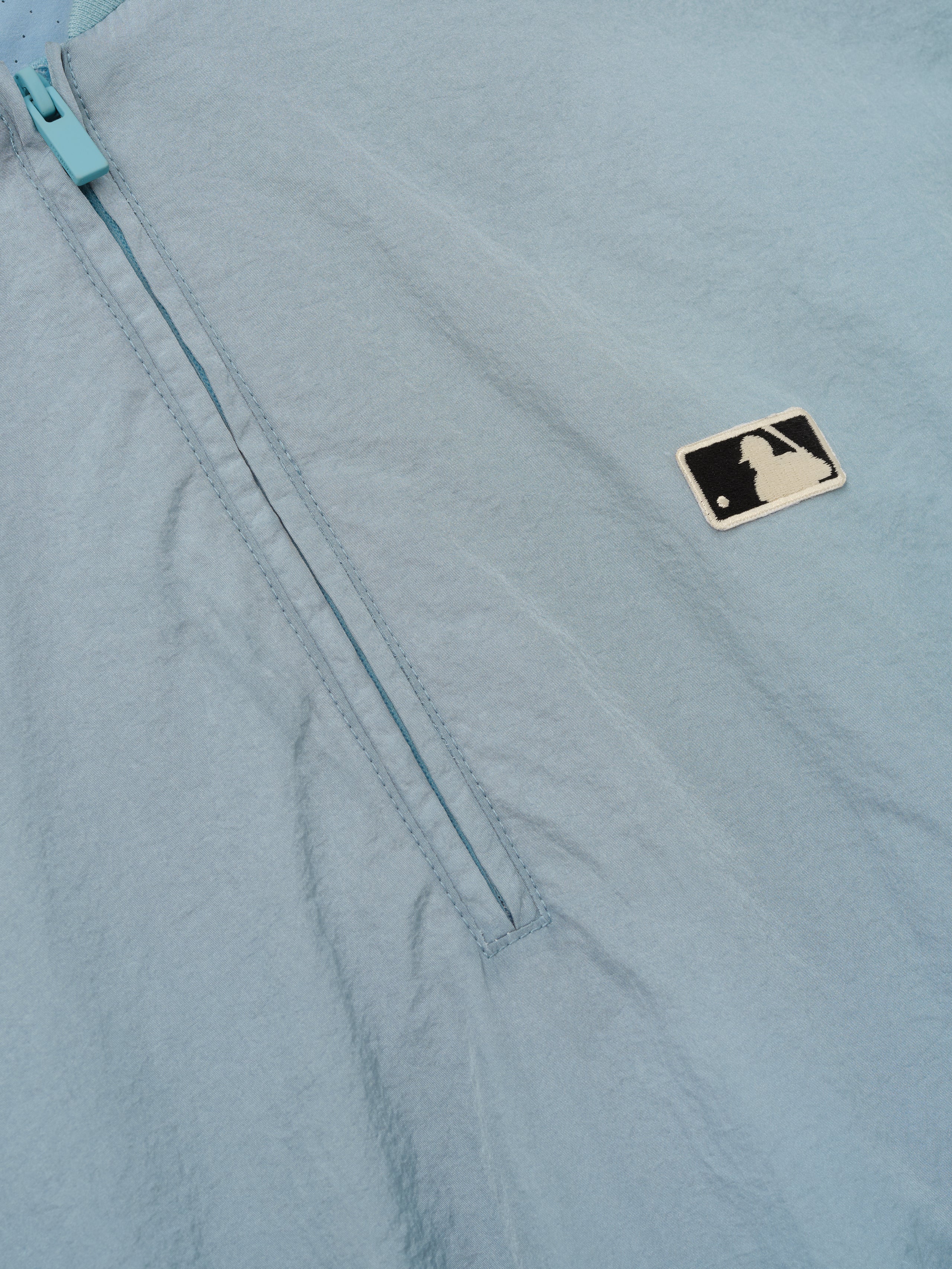 Close-up of the Mlb 3/4 Sleeve Pullover in soft blue showing a partially zipped quarter-zip with matching zipper and a small contrasting logo patch on lightweight fabric.