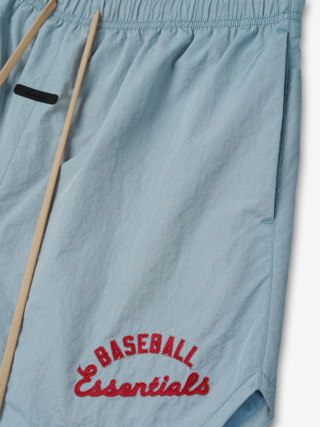 Mlb Gym Short in light stone blue featuring beige drawstrings and red embroidered "Baseball Essentials" text near the hem on lightweight athletic bottoms.