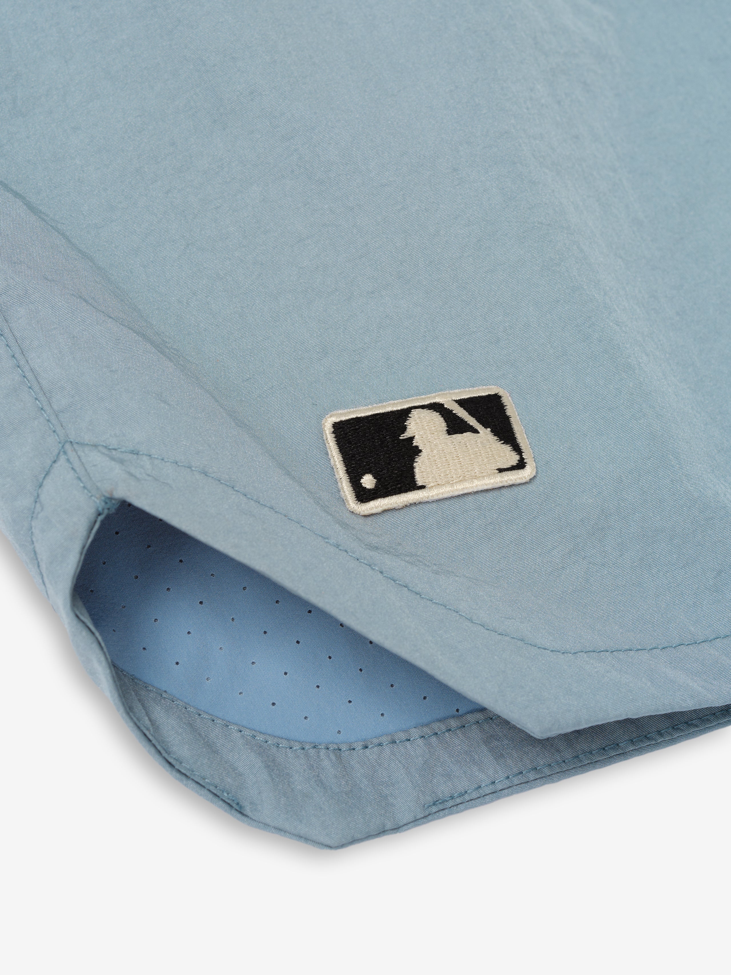 Close-up of the hem on Mlb Gym Short in stone blue featuring a breathable perforated inner lining and a small stitched black and cream baseball batter logo patch.
